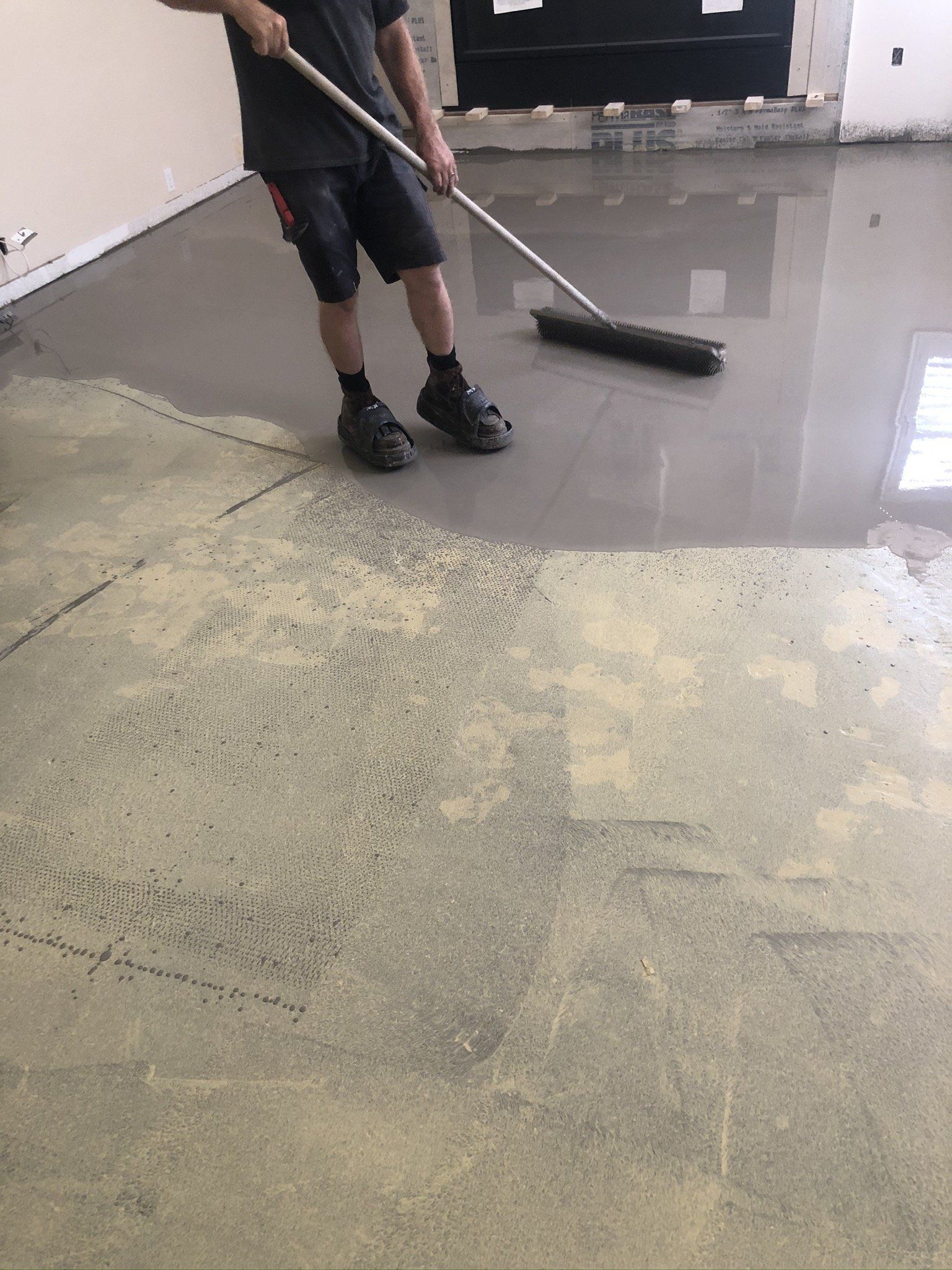 Person sweeping a dusty concrete floor in a bare room under renovation