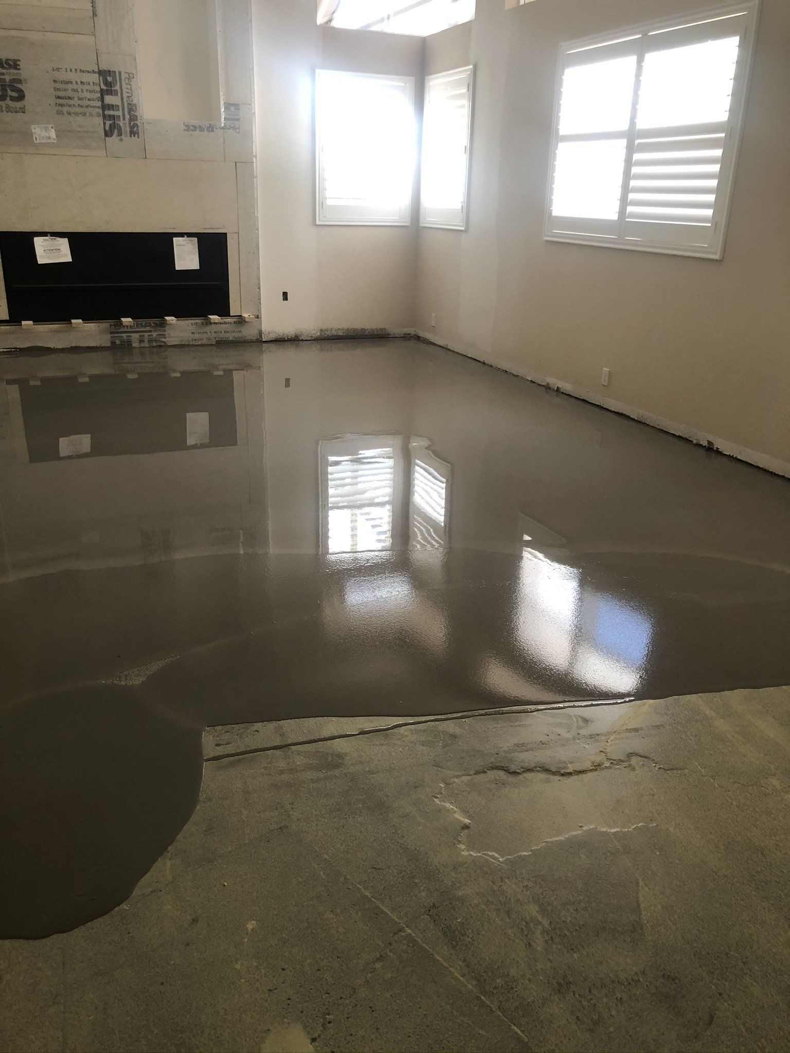 Empty room with glossy concrete floor, unfinished walls, and sunlight from two windows