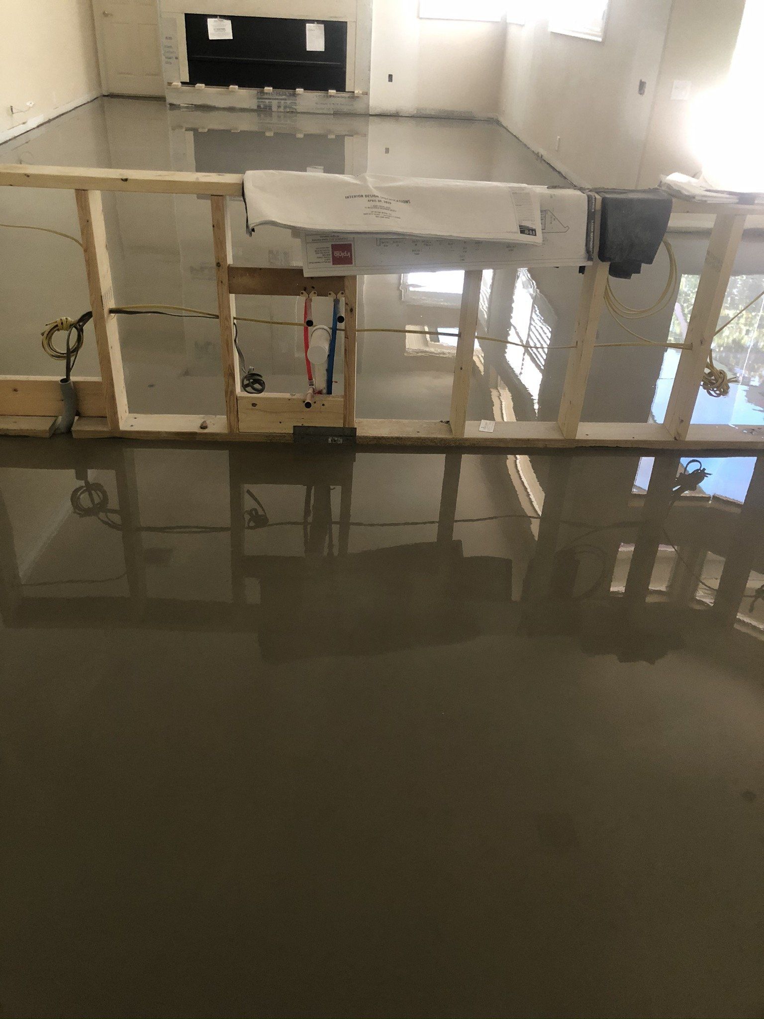 Flooded kitchen with standing water, unfinished cabinets, and a sink under a window.