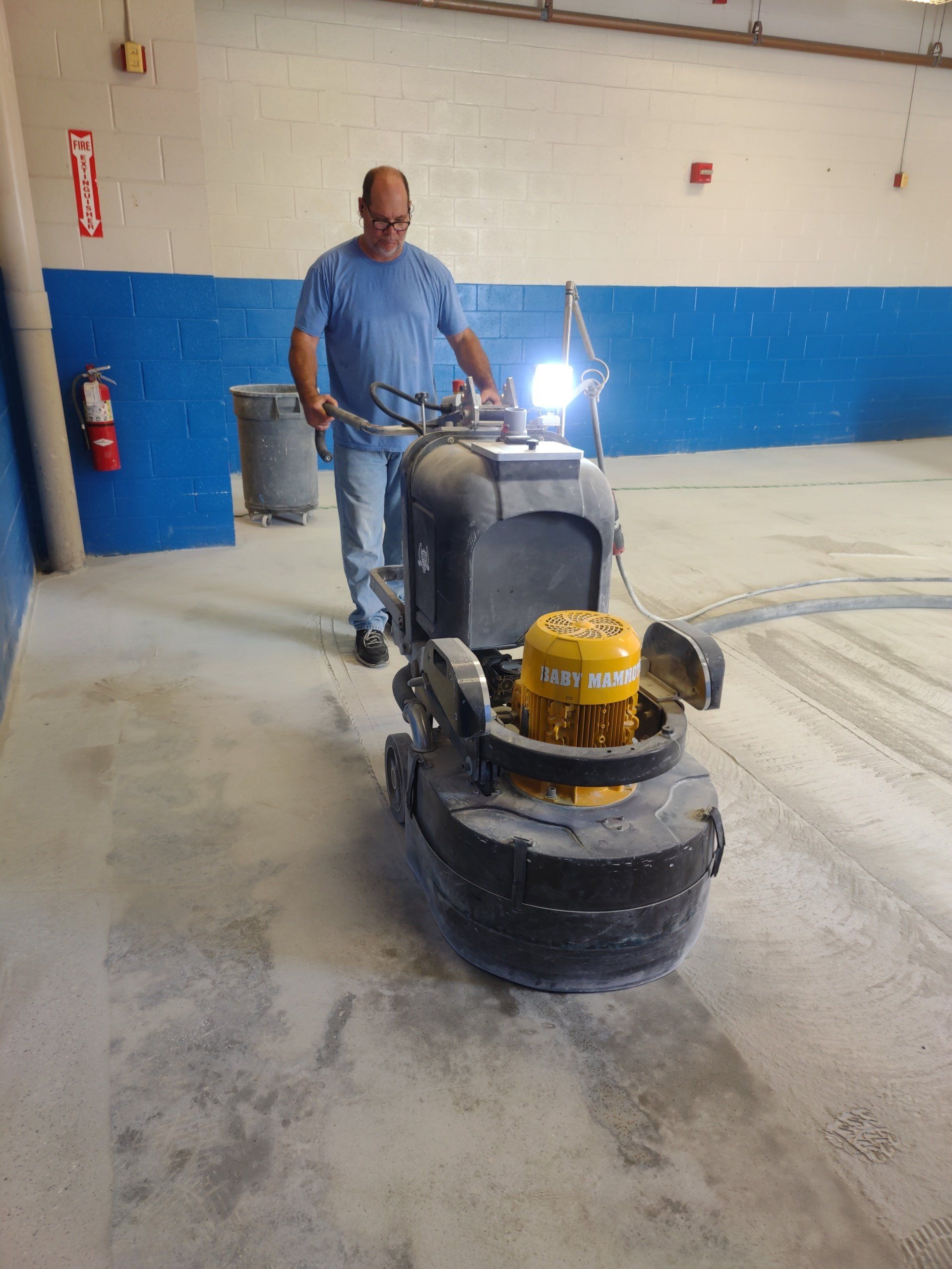Worker operating a floor grinder in a dusty indoor space with blue and white walls