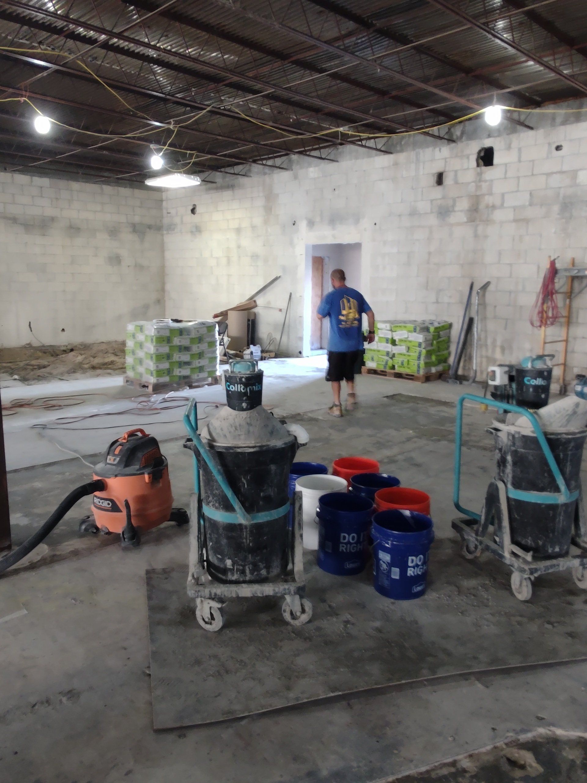 Construction site interior with concrete walls, tools, buckets, and a worker in a blue shirt