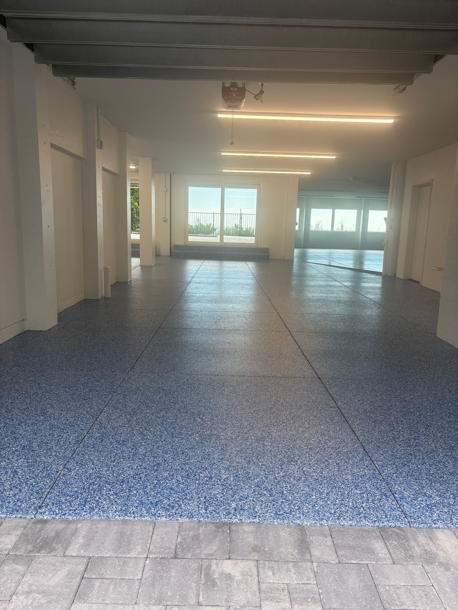 Empty indoor space with blue-speckled floor, white walls, and large windows at the far end