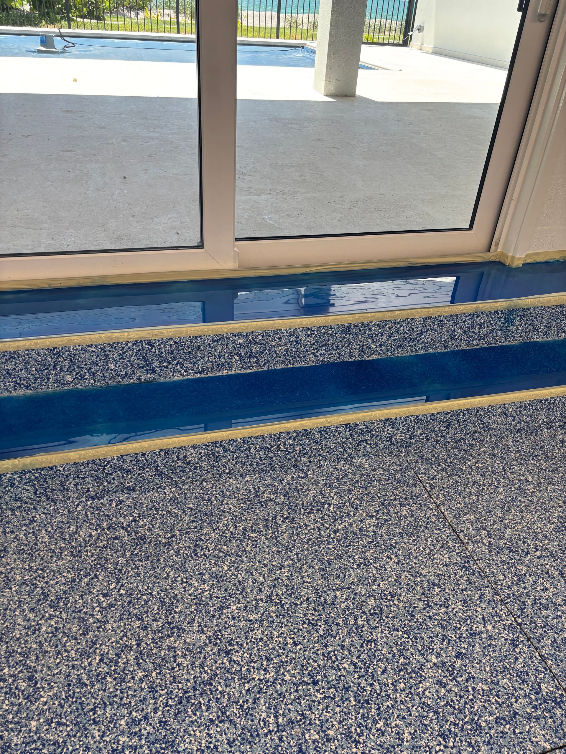 Indoor carpet edge by glass doors, with blue threshold strip and pebbled outdoor walkway beyond.