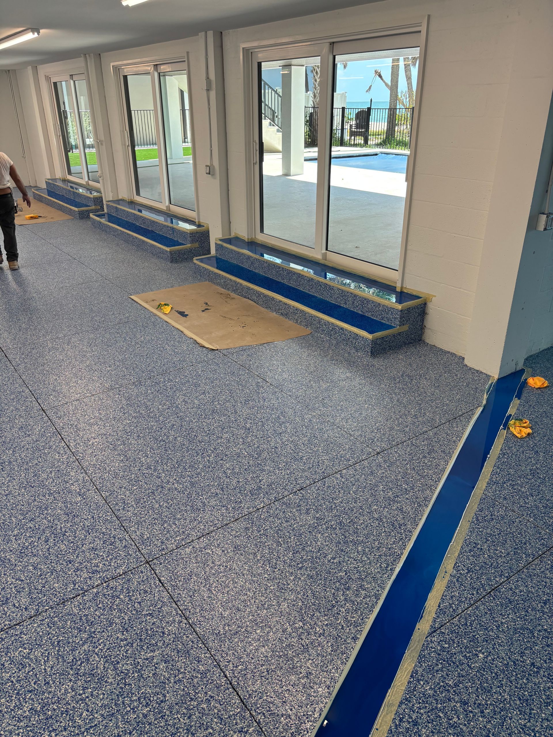 Empty indoor lobby with blue-speckled floor, glass doors, and a blue bench along the wall.