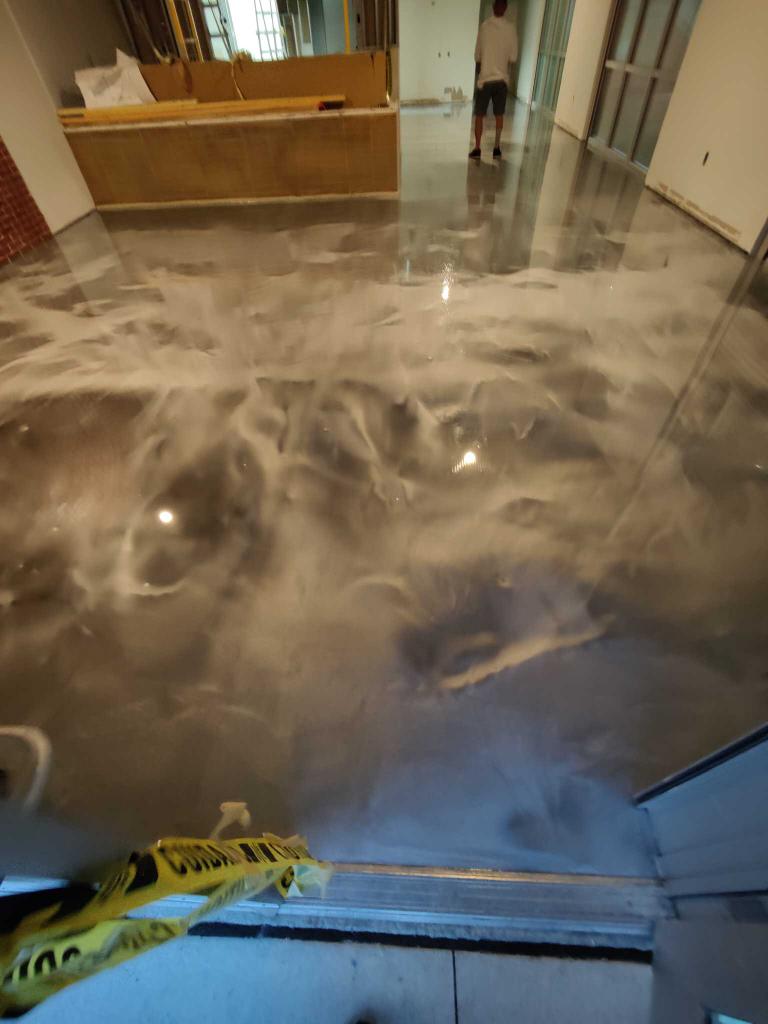 Polished concrete floor with swirling reflections in a bright indoor space, near a yellow caution tape barrier