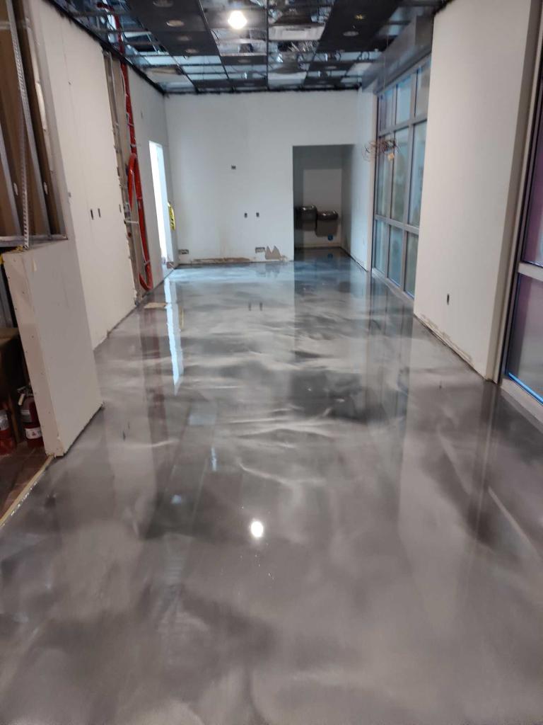 Empty hallway with glossy concrete floor, white walls, and exposed ceiling in a building under construction