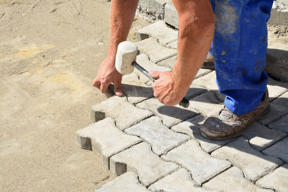 A Man is Using a Rubber Mallet to Hammer Bricks on a Sidewalk — Tiger Concrete ACT In Fadden, ACT