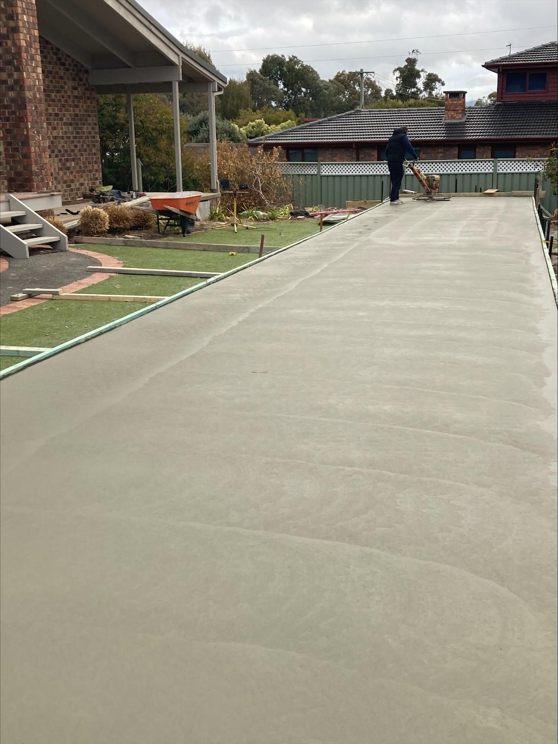 A Man Is Working On A Concrete Driveway In Front Of A House — Tiger Concrete ACT In Fadden, ACT