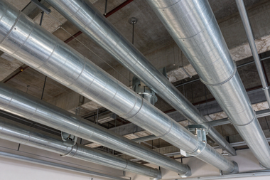 Silver ventilation ducts running across an unfinished industrial ceiling