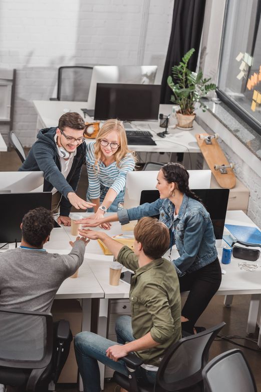 Colleagues gathered around a table in a bright office, stacking hands in a team huddle