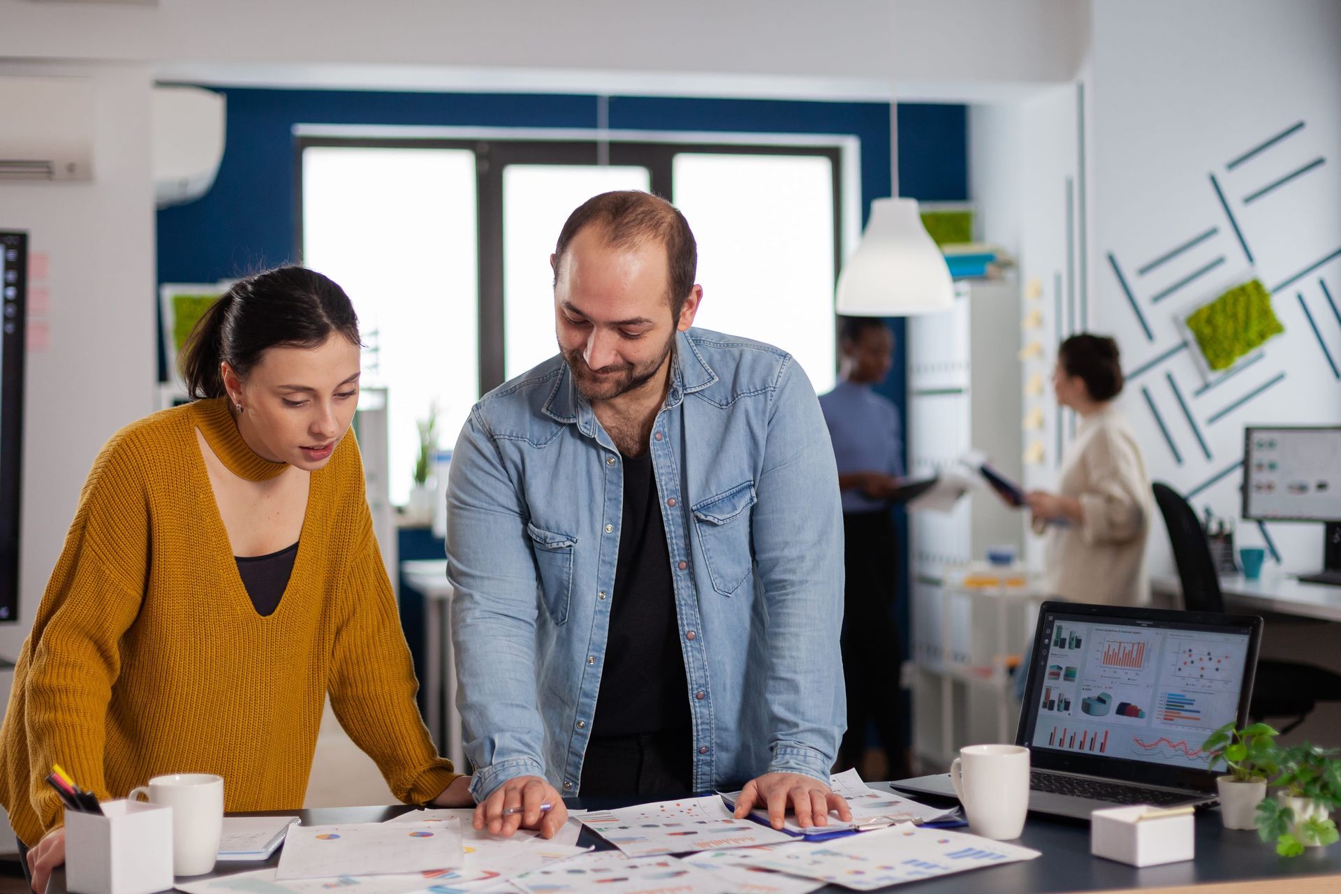 Two coworkers lean over design sketches in a bright office, reviewing plans at a table.