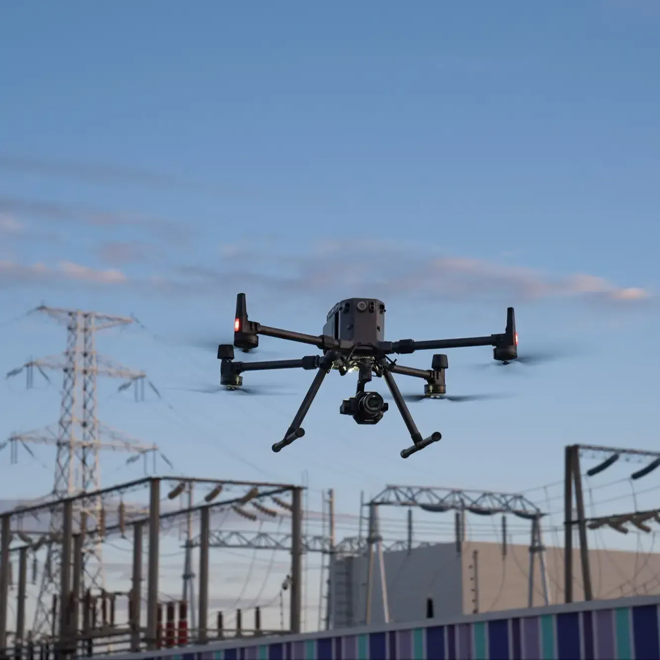 Industrial drone flying above a fenced electrical substation at dusk