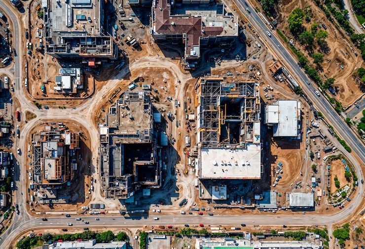 Aerial view of a large construction site with multiple buildings, cranes, and dirt roads.