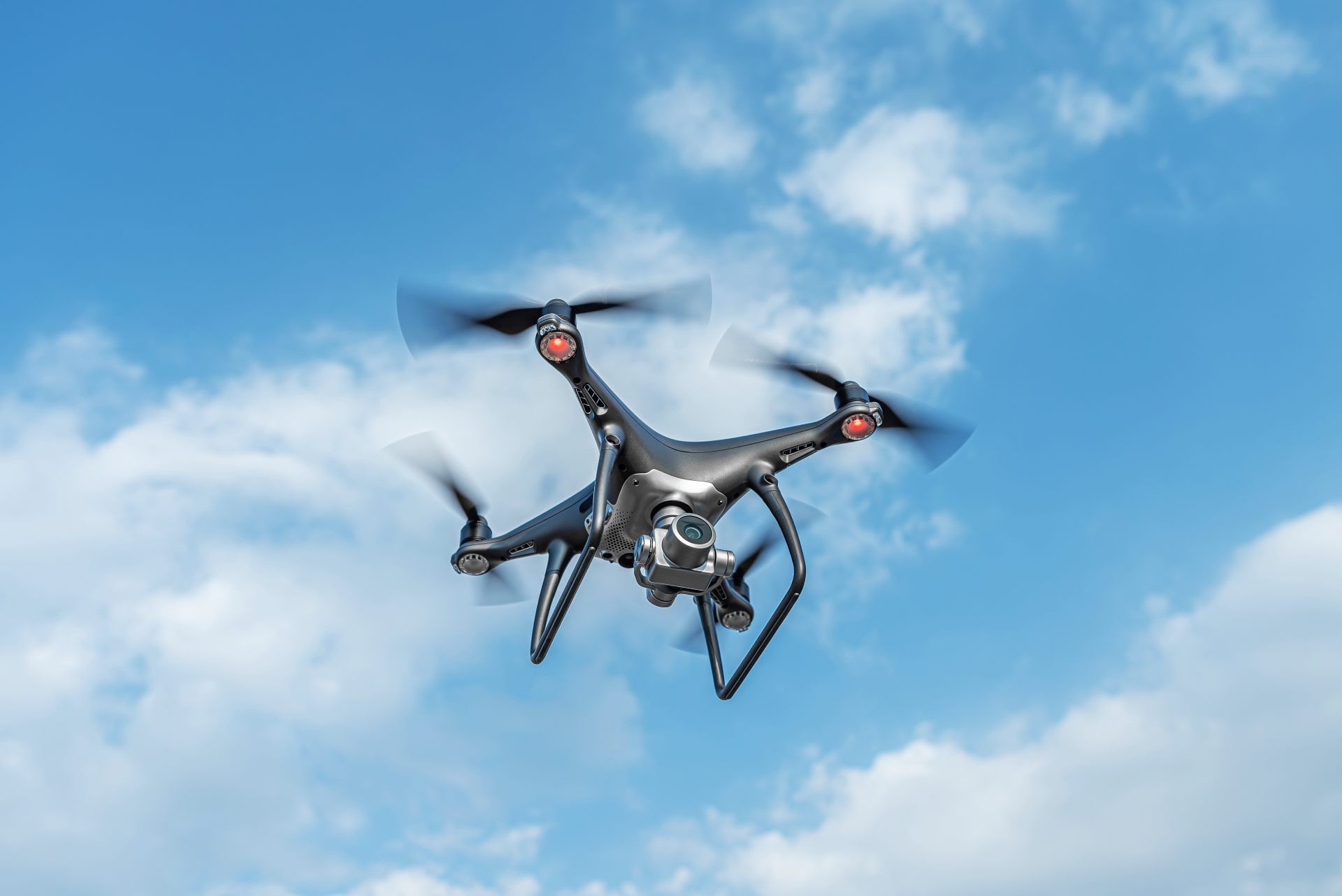 A drone flies over a city at twilight, shining a bright spotlight down onto the buildings below.