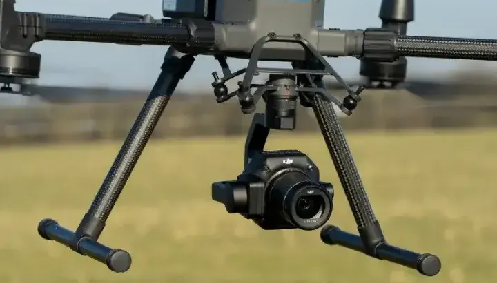 Black camera drone hovering over a field with a mounted gimbal camera