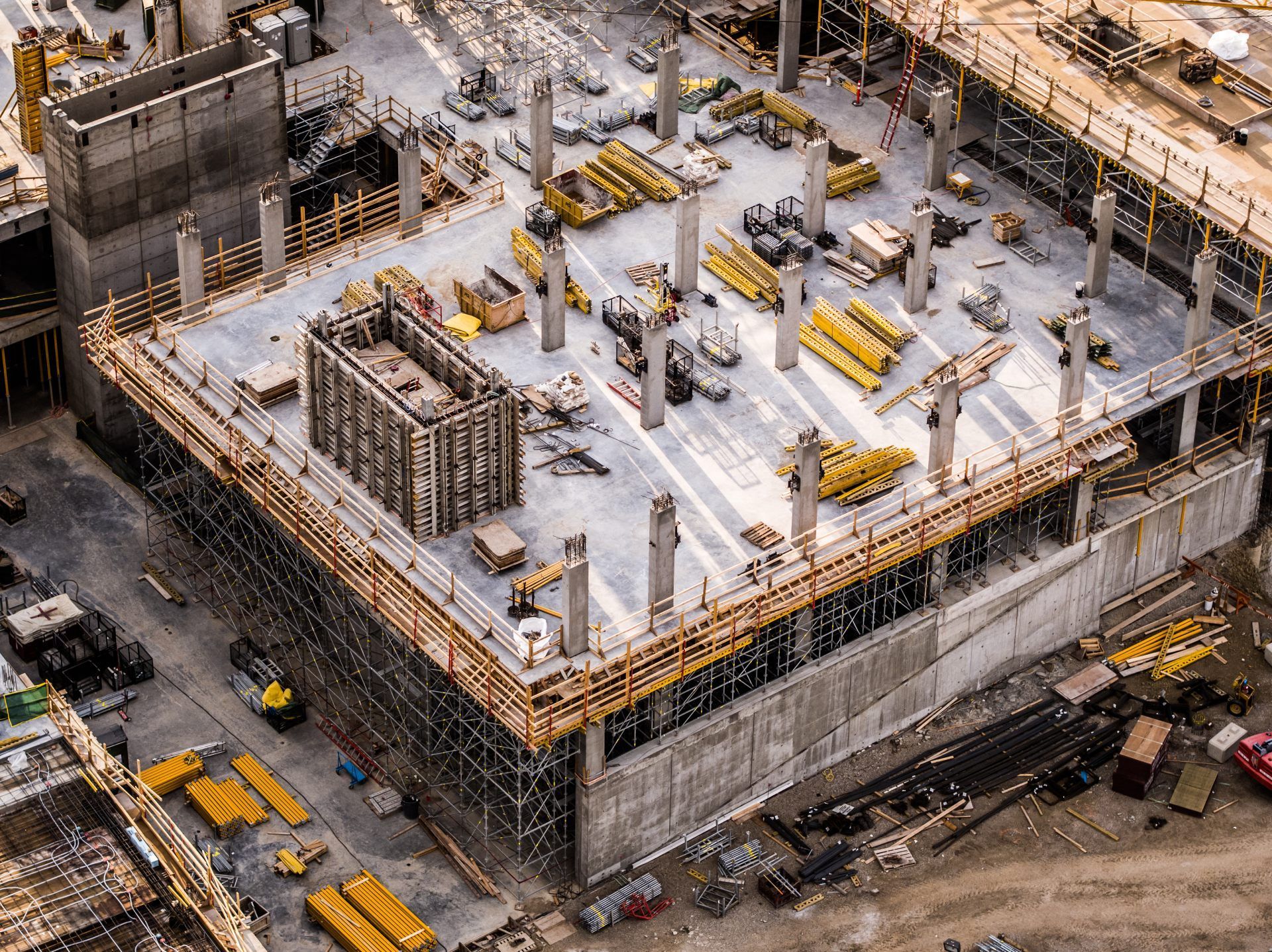 Aerial view of a concrete building under construction with scaffolding and yellow equipment