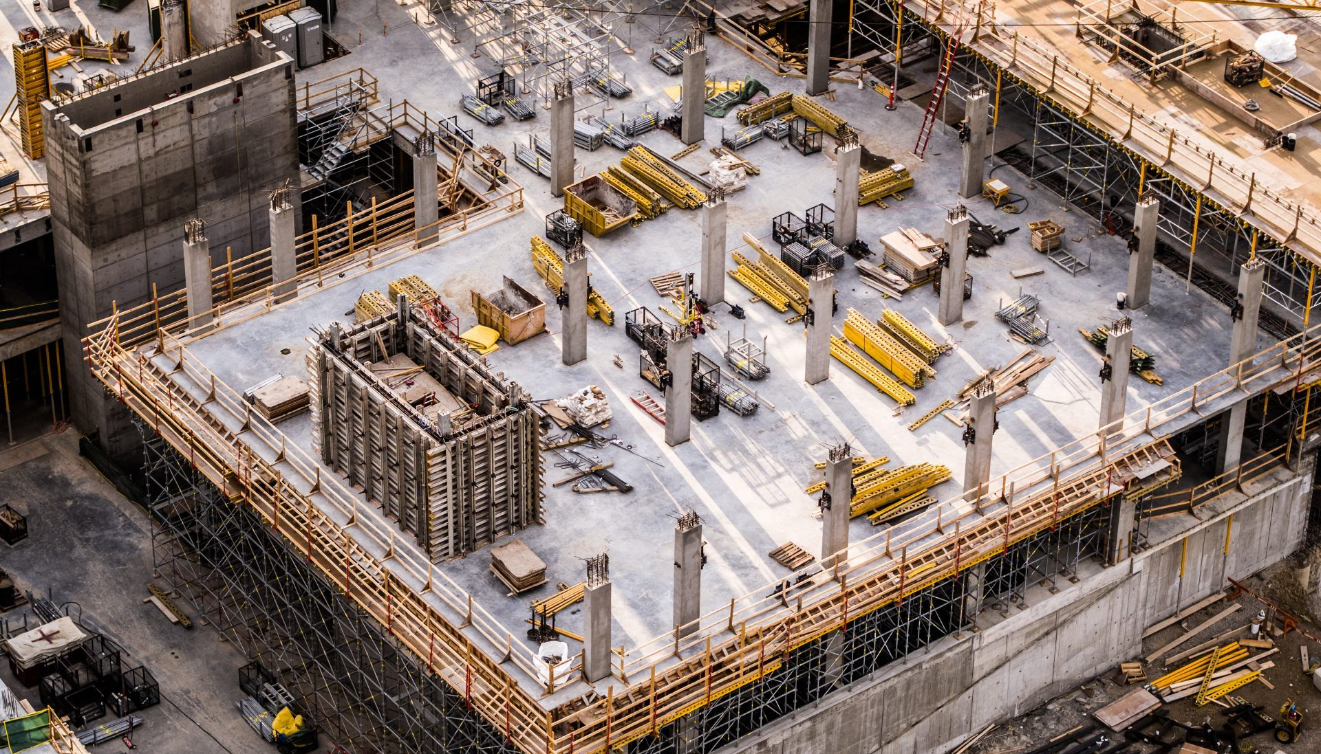 Aerial view of a large concrete construction site with scaffolding, columns, and yellow equipment.