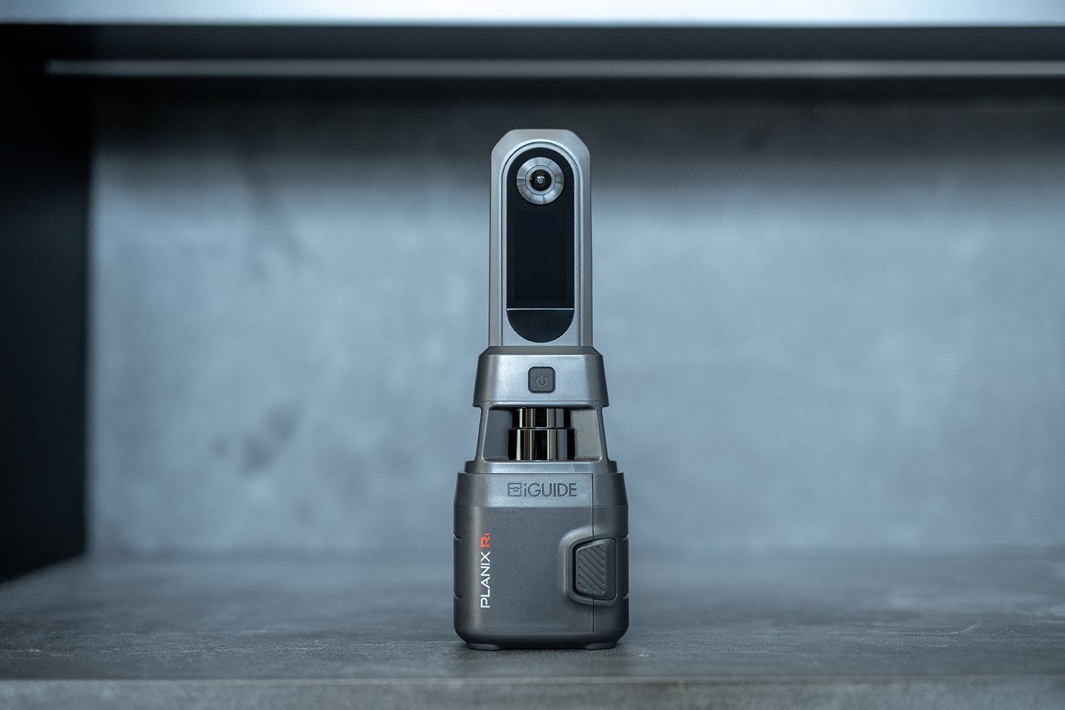 Small gray handheld device standing upright on a metallic surface in a dim industrial setting