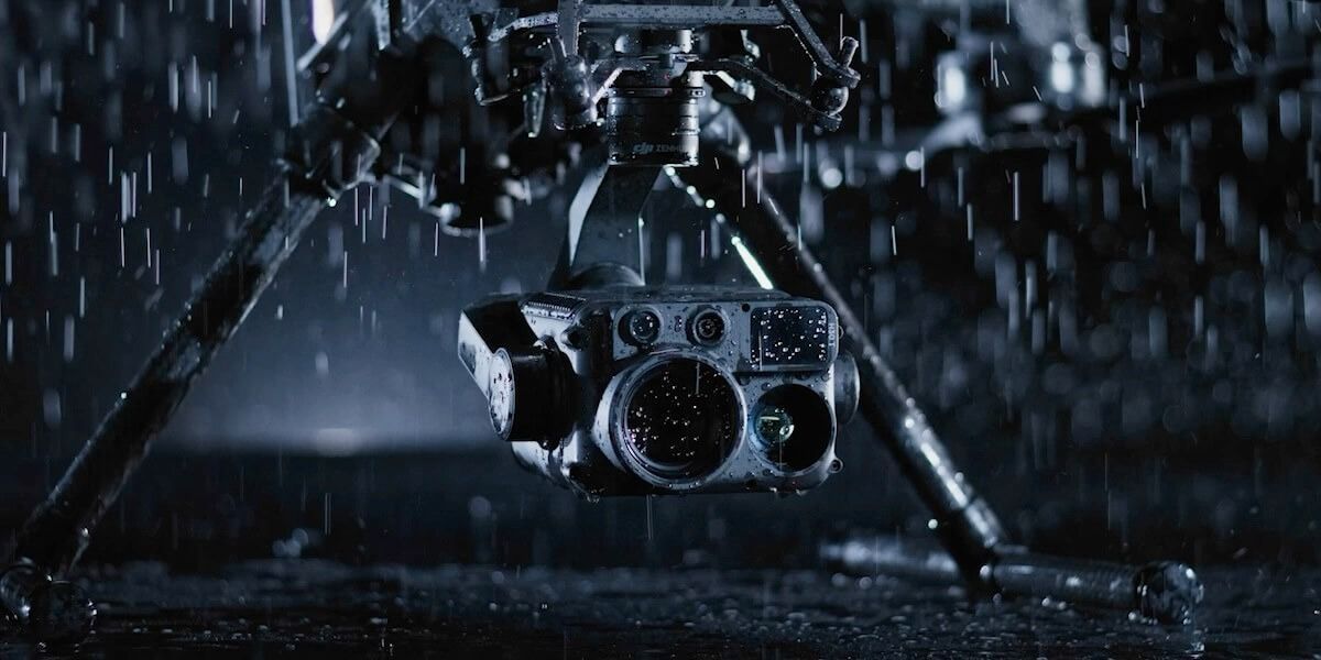 A professional video camera on a tripod faces a blurred crowd, with the text