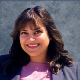 A woman wearing a pink shirt and a black jacket smiles for the camera