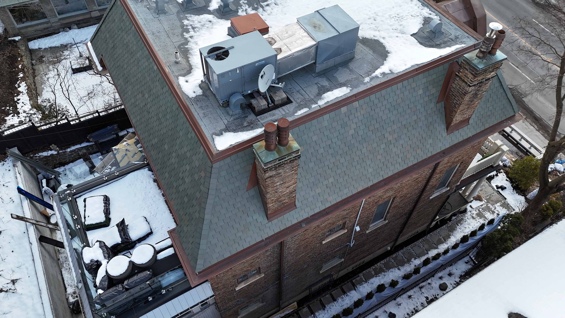 Vue aérienne d'un bâtiment en briques avec un toit gris, des unités de climatisation sur le toit et de la neige autour.