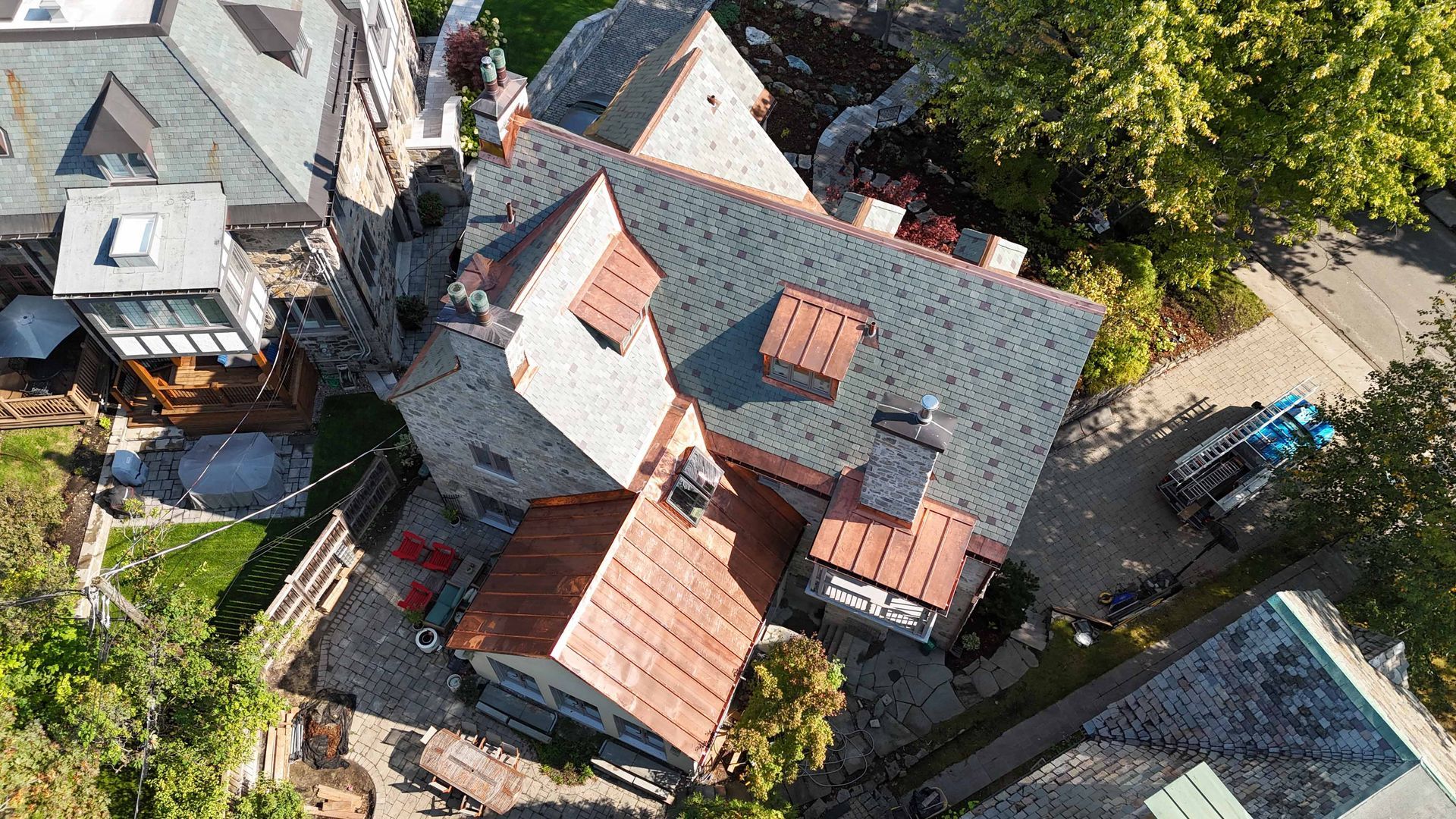 Vue aérienne d'une petite maison d'habitation aux toits rouges, entourée d'arbres et de maisons voisines.