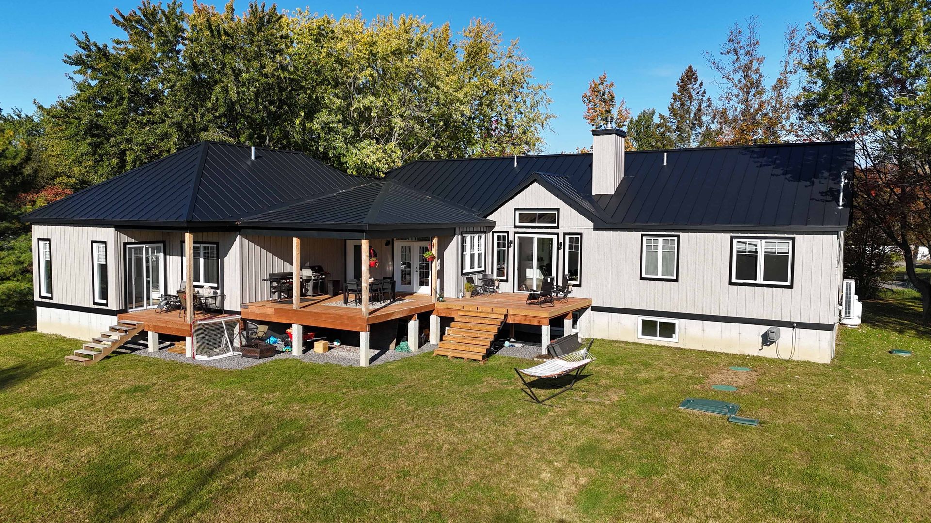 Maison blanche de plain-pied avec toit noir et terrasse en bois, vue depuis le jardin par une journée ensoleillée.