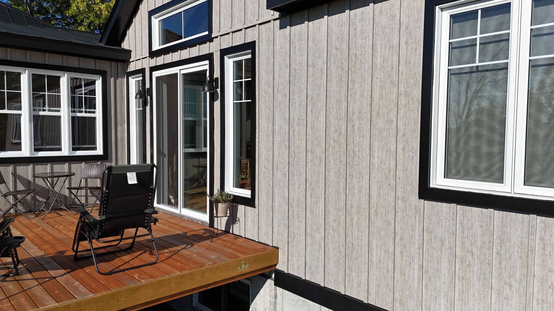 Terrasse en bois jouxtant une maison aux fenêtres à cadre noir et une chaise de patio sous un ciel lumineux