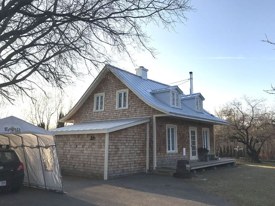 Une maison en brique avec un toit en métal et une voiture garée devant.
