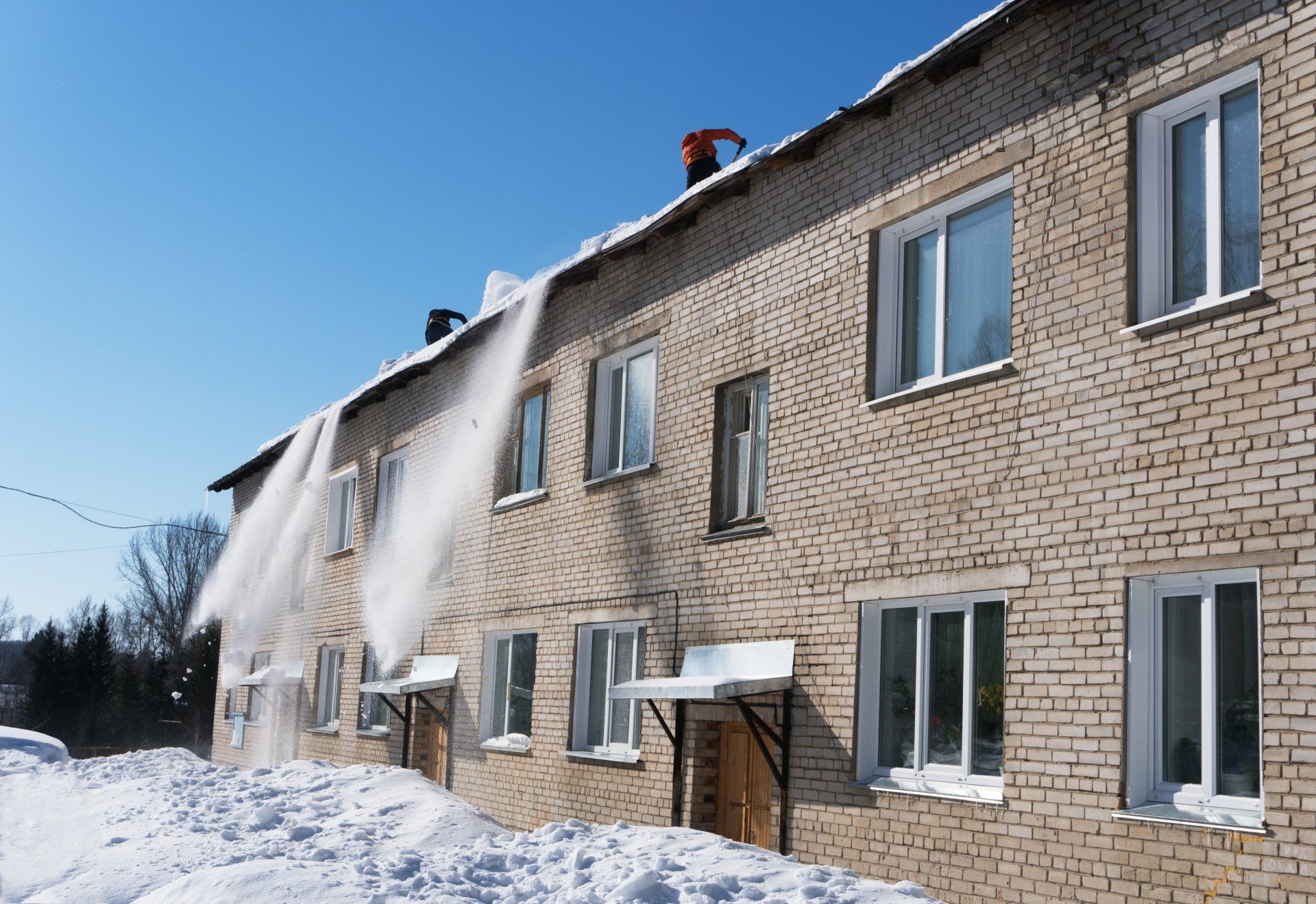 Un homme déneige le toit d'un bâtiment en brique