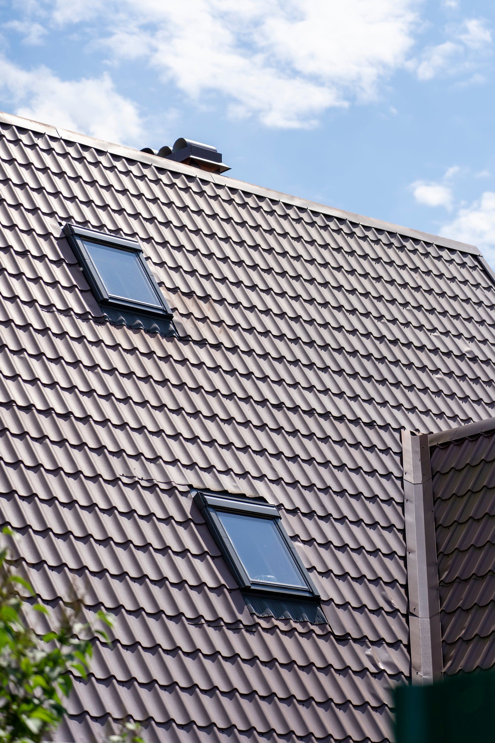 Toit de maison en tuiles brunes avec deux fenêtres de toit sur fond de ciel bleu