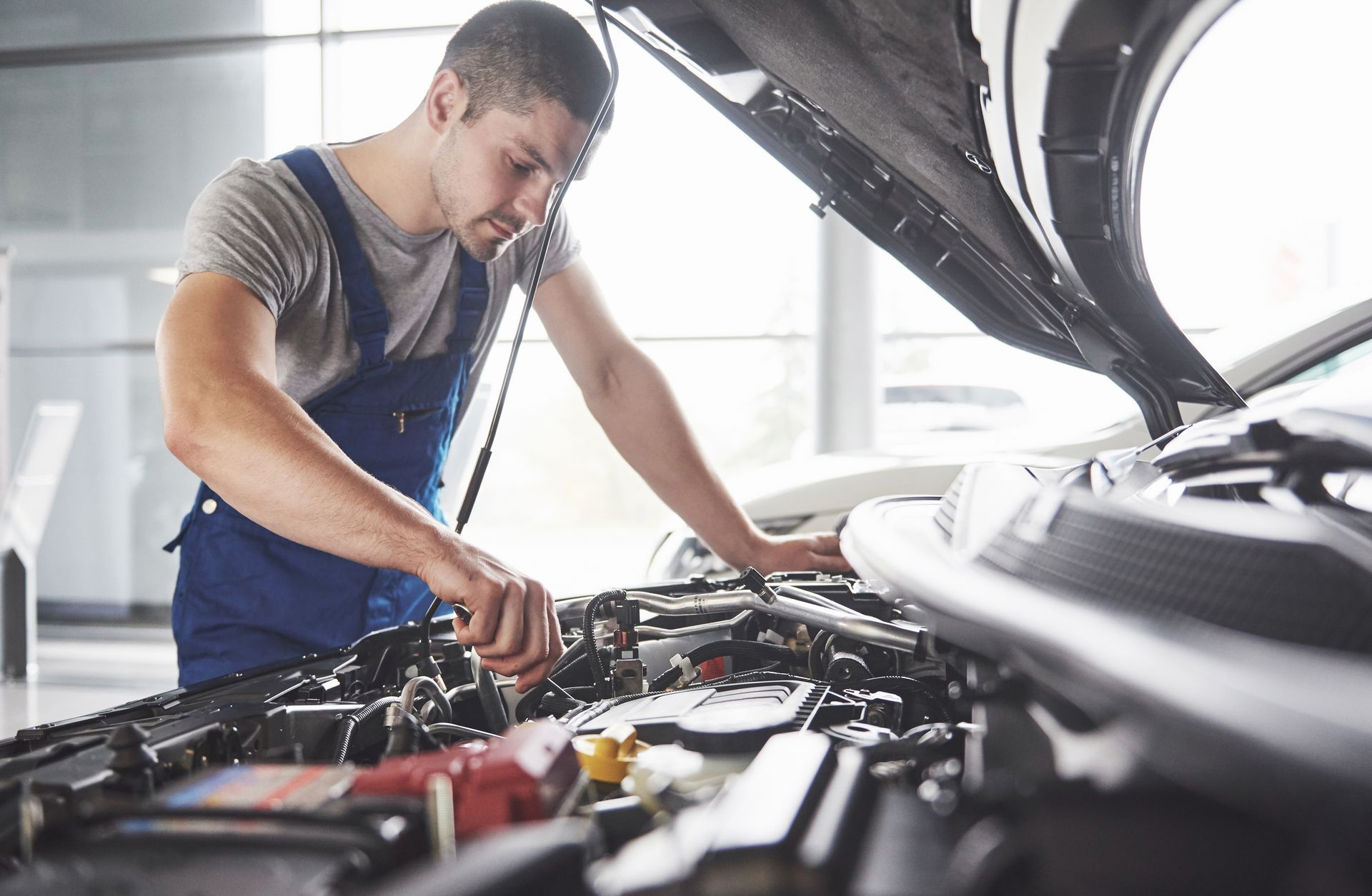 Person checking car engine under open hood, performing vehicle maintenance outdoors on driveway lawn. Person checking car engine under open hood, performing vehicle maintenance outdoors on driveway lawn.