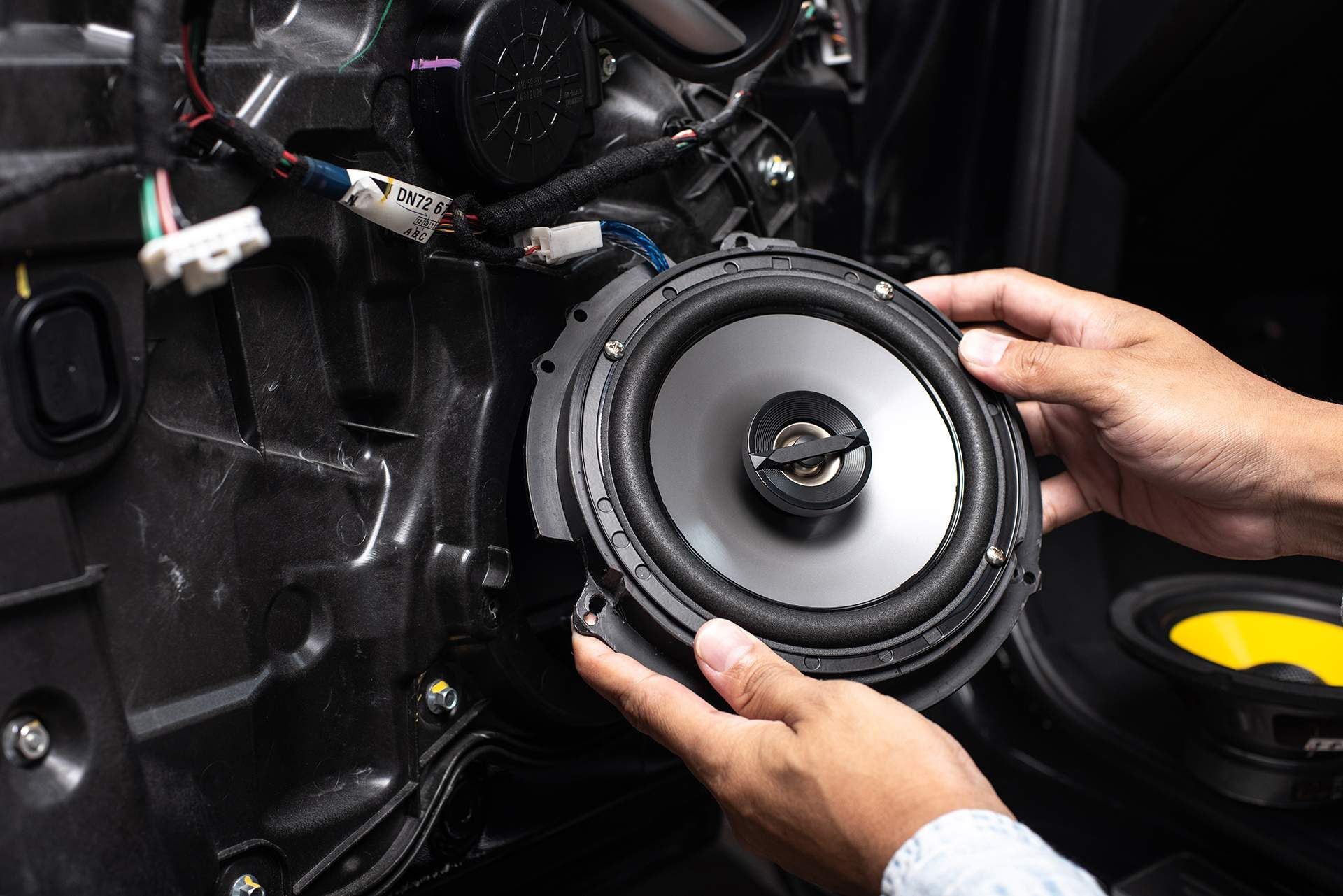 A person is holding a speaker in their hands in front of a car.