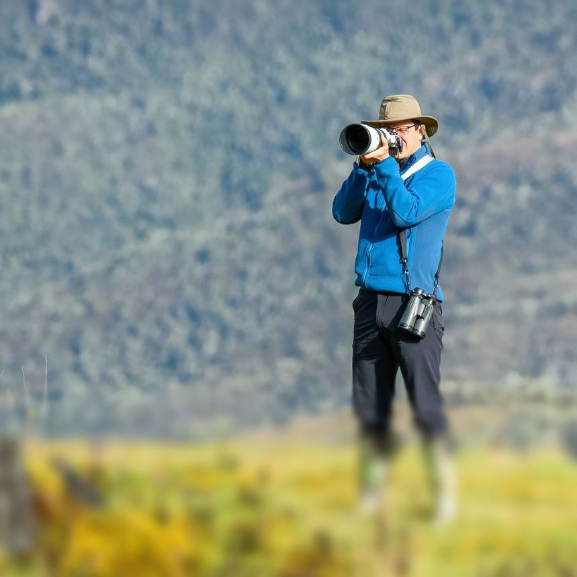 A man is standing in a field taking a picture with a camera.
