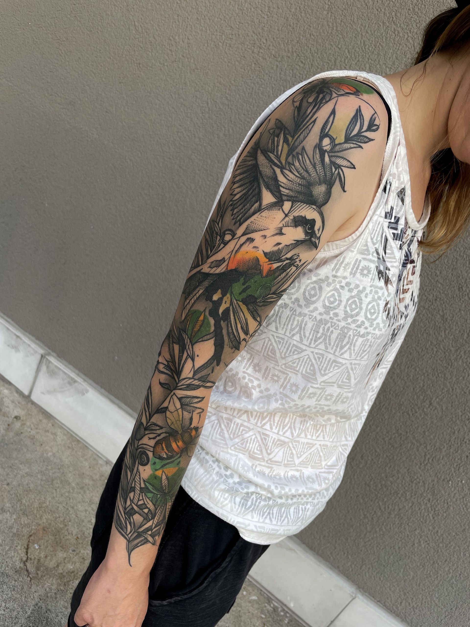 Person with a full sleeve tattoo featuring a fox and floral elements; wearing a white tank top, standing.