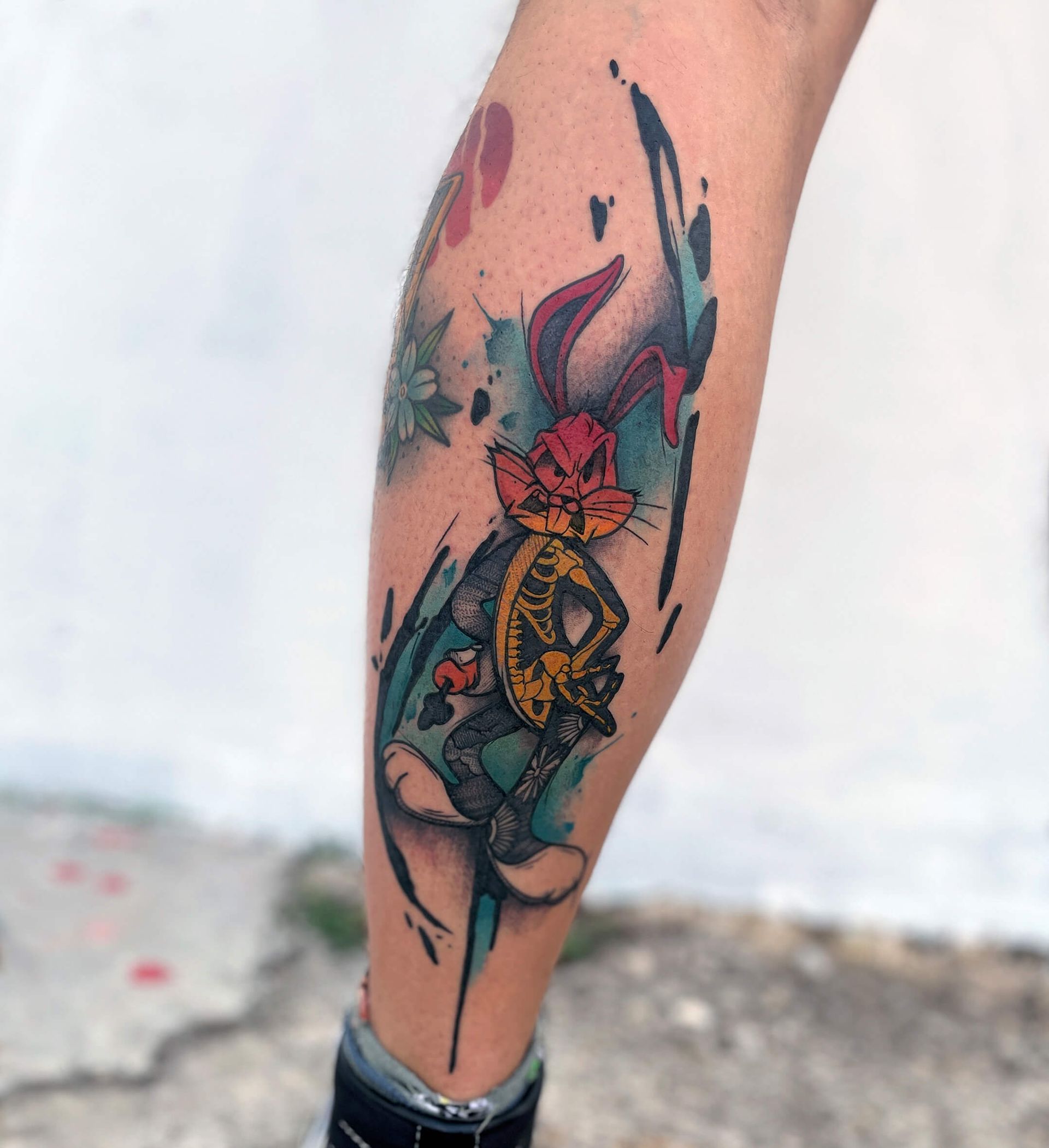 Beintattoo von Bugs Bunny mit Aquarellspritzern in Blau, Rot und Gelb.