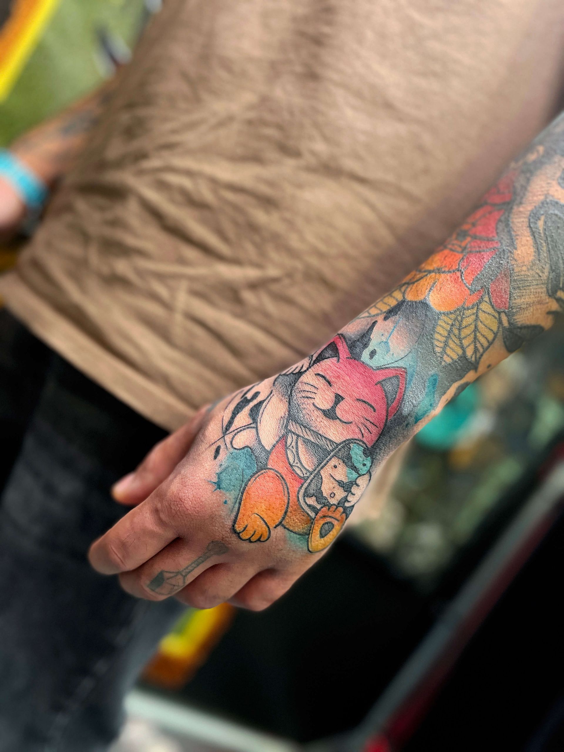 Buntes Katzentattoo auf der Hand und dem Arm einer Person, umgeben von floralen und abstrakten Mustern.