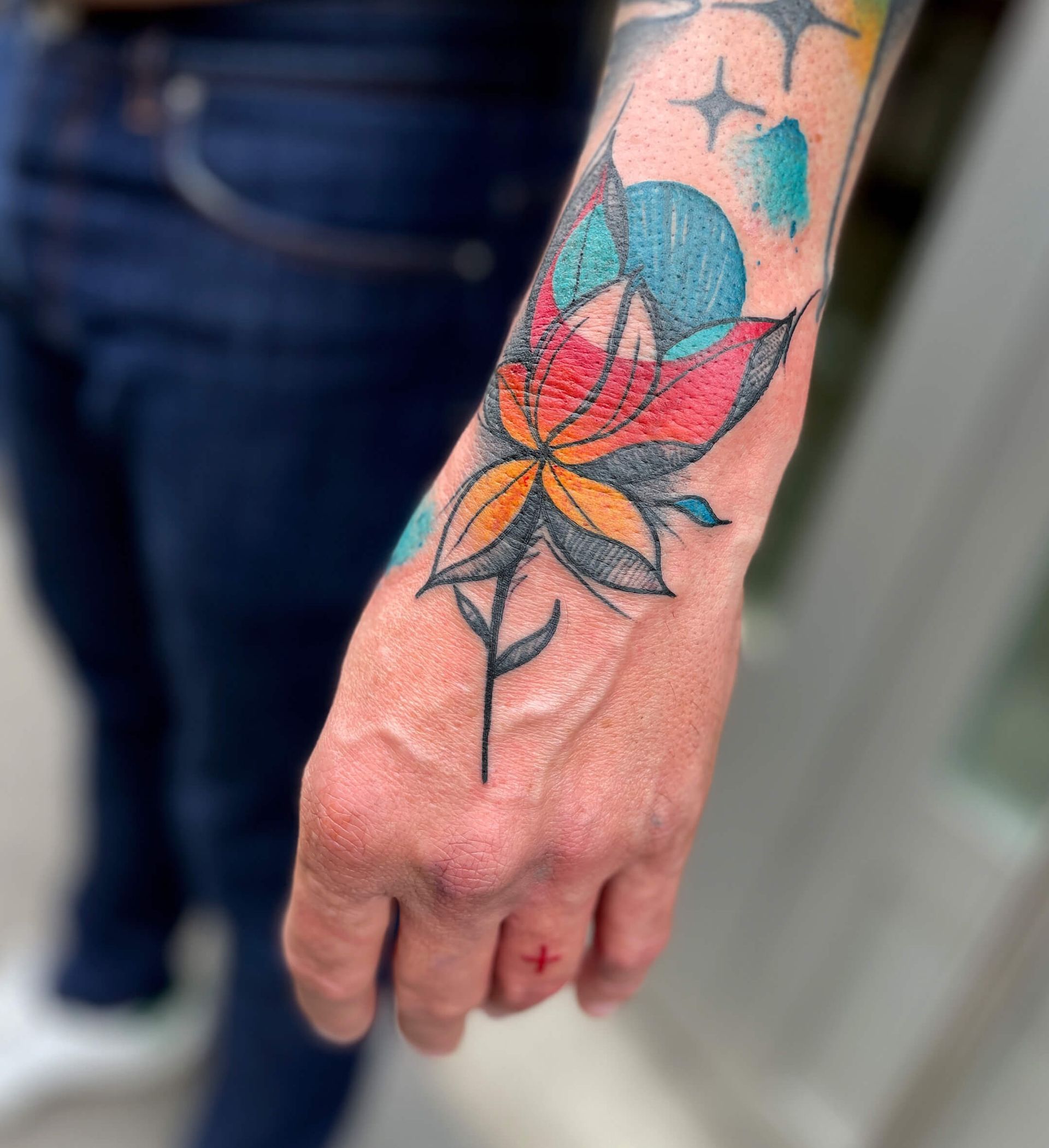 Tätowierung einer bunten Blume und einer blauen Kugel am Handgelenk einer Person.