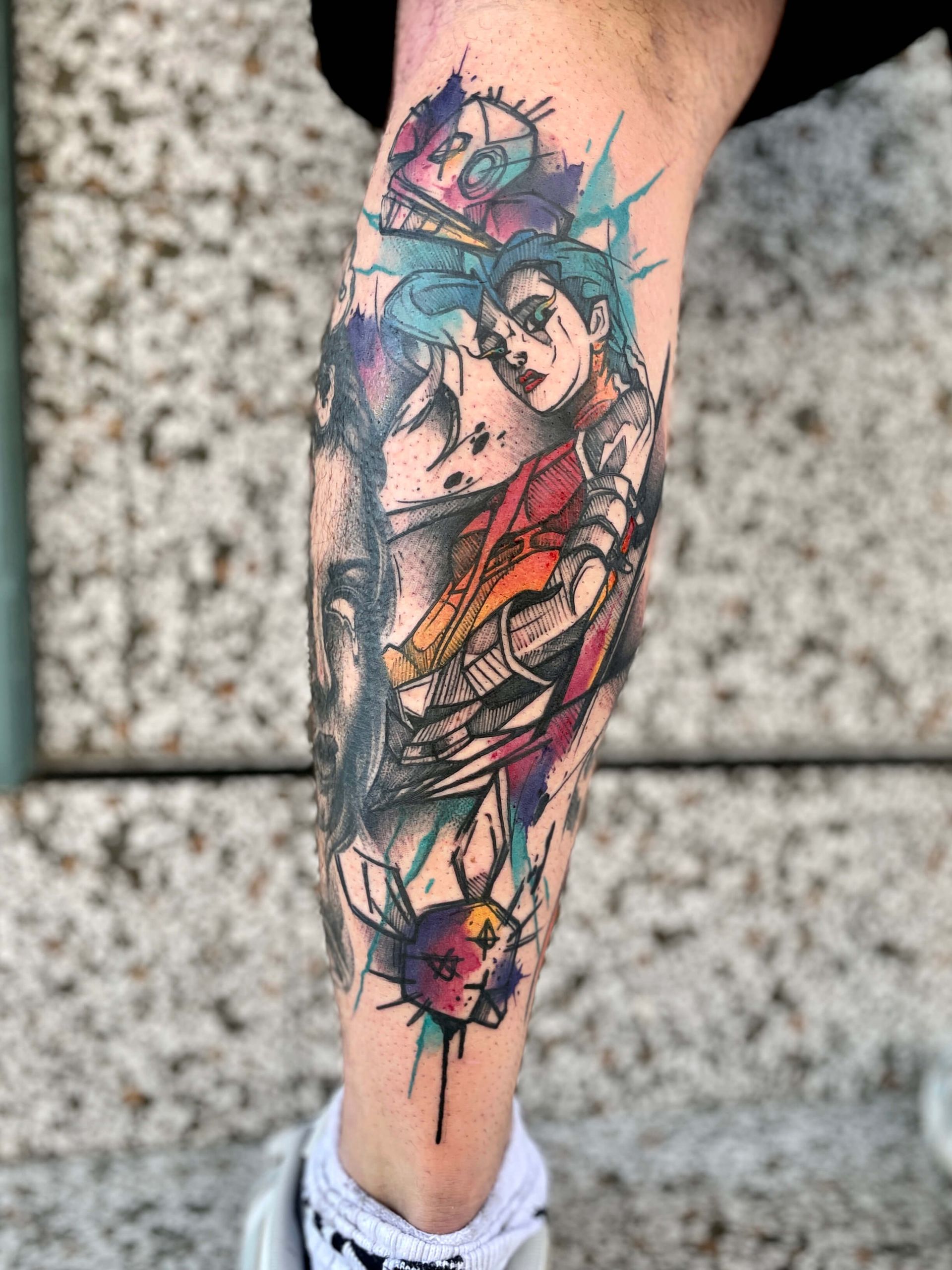 Buntes Tattoo des Beins einer Person. Das Kunstwerk zeigt ein stilisiertes Porträt mit Tintenspritzern und Farbklecksen.