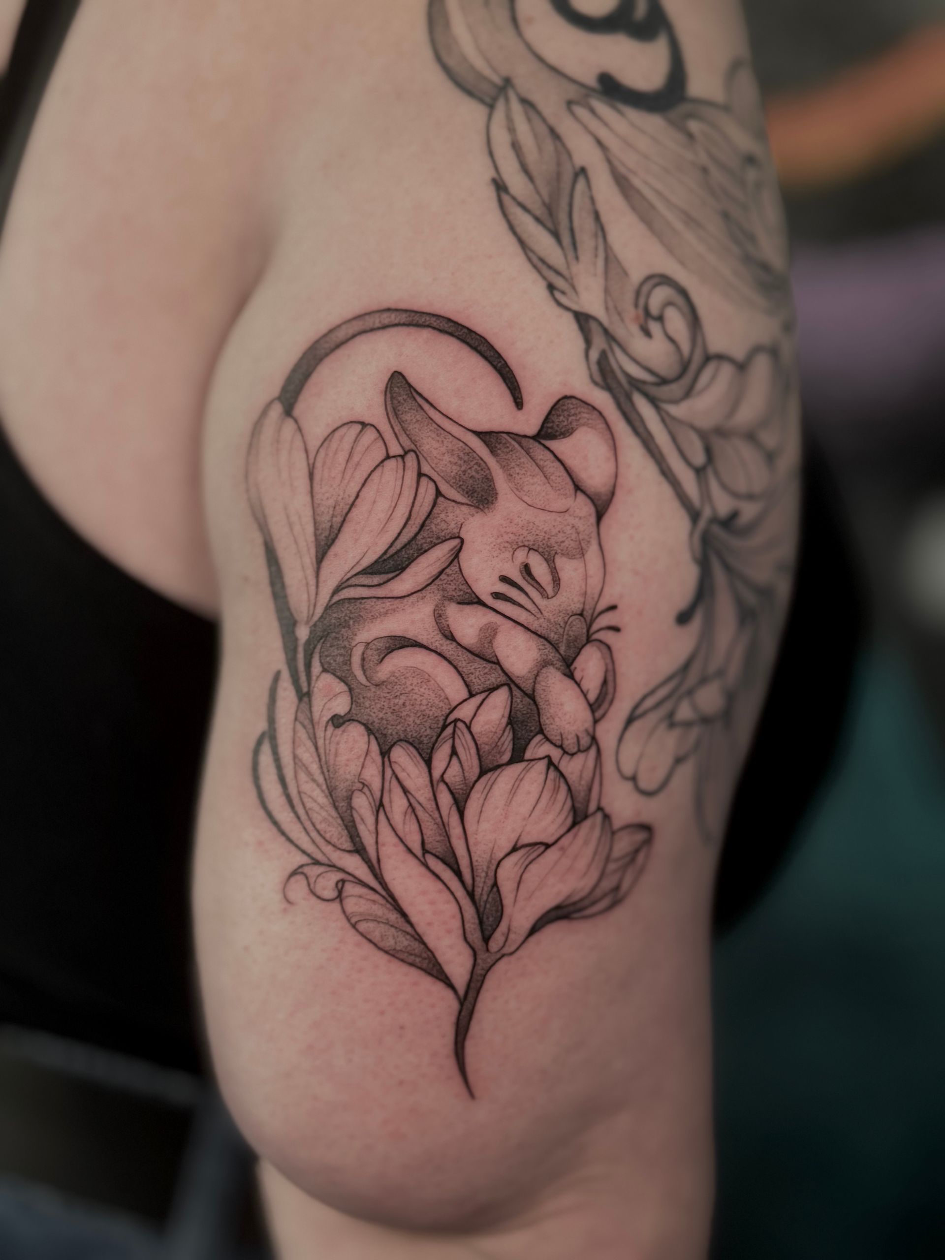 Tätowierung einer schlafenden Maus, eingebettet in stilisierte Blumen, auf einem Arm, schwarze Tinte.