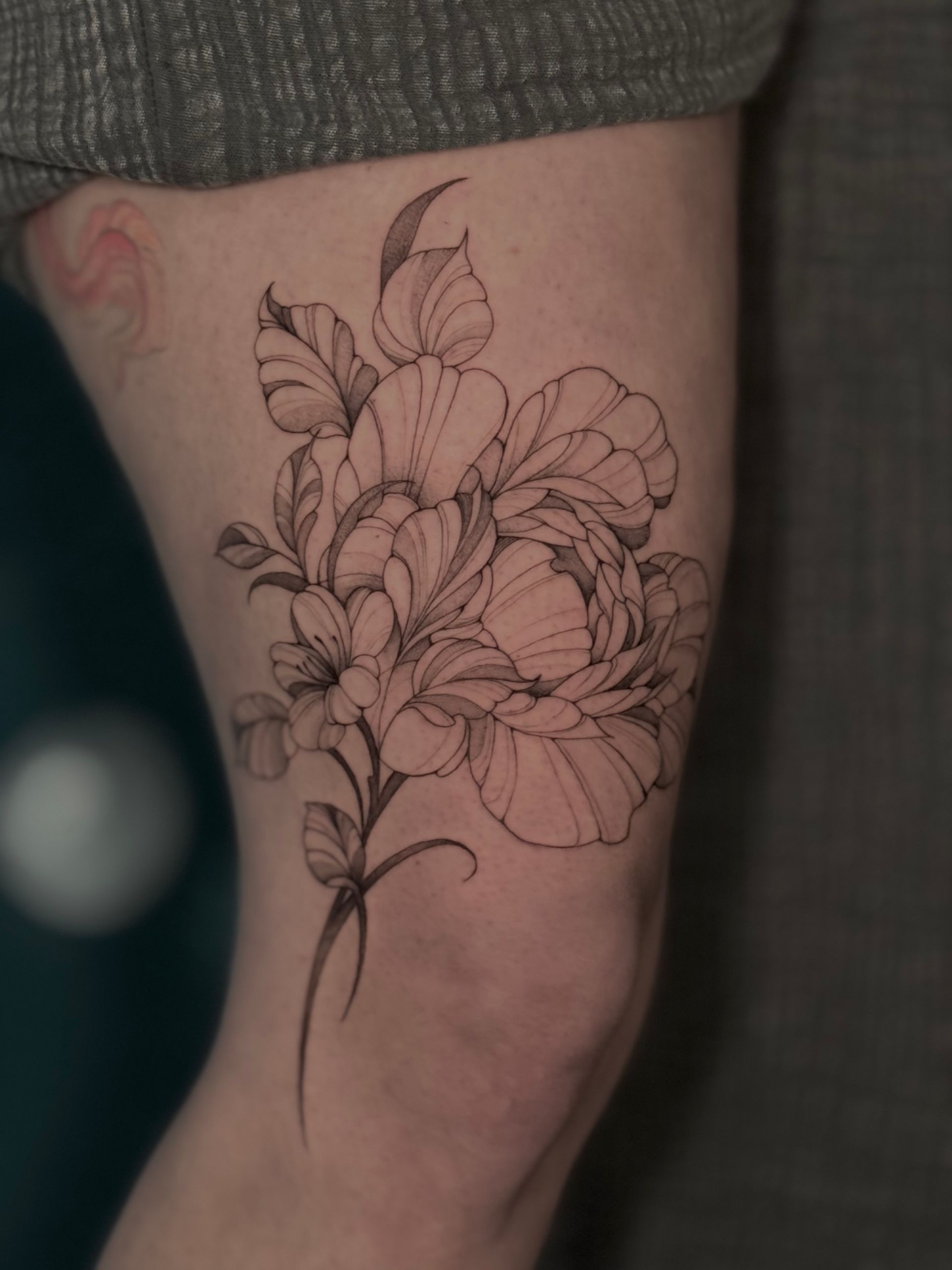 Schwarzes, linienförmiges Blumentattoo auf Oberschenkel und Knie. Blüten und Blätter an einem schlanken Stiel.