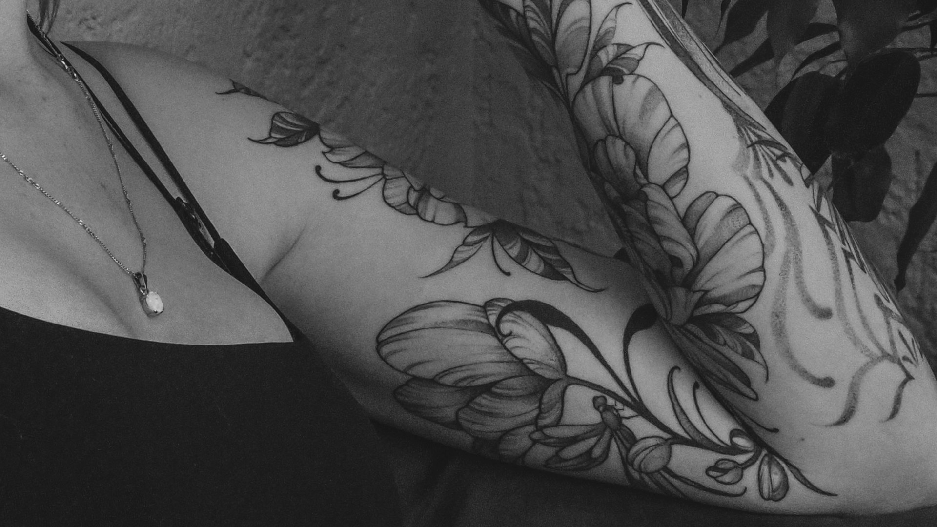 Schwarz-weißes Blumentattoo auf dem Arm einer Person, neben einem Button-Down-Hemd.