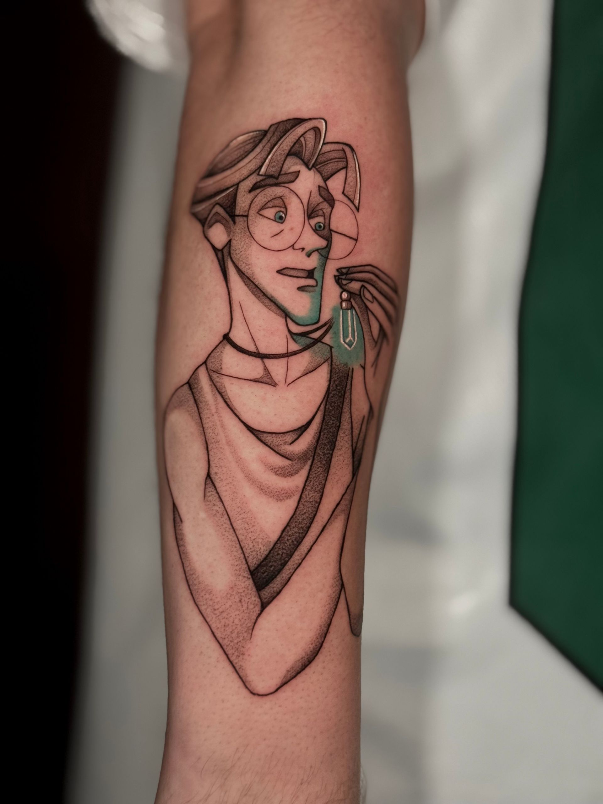 Das Tattoo auf seinem Arm zeigt einen Mann aus Disneys „Atlantis“, der einen leuchtend blauen Anhänger hält. Er trägt eine Brille und ein ärmelloses Oberteil.