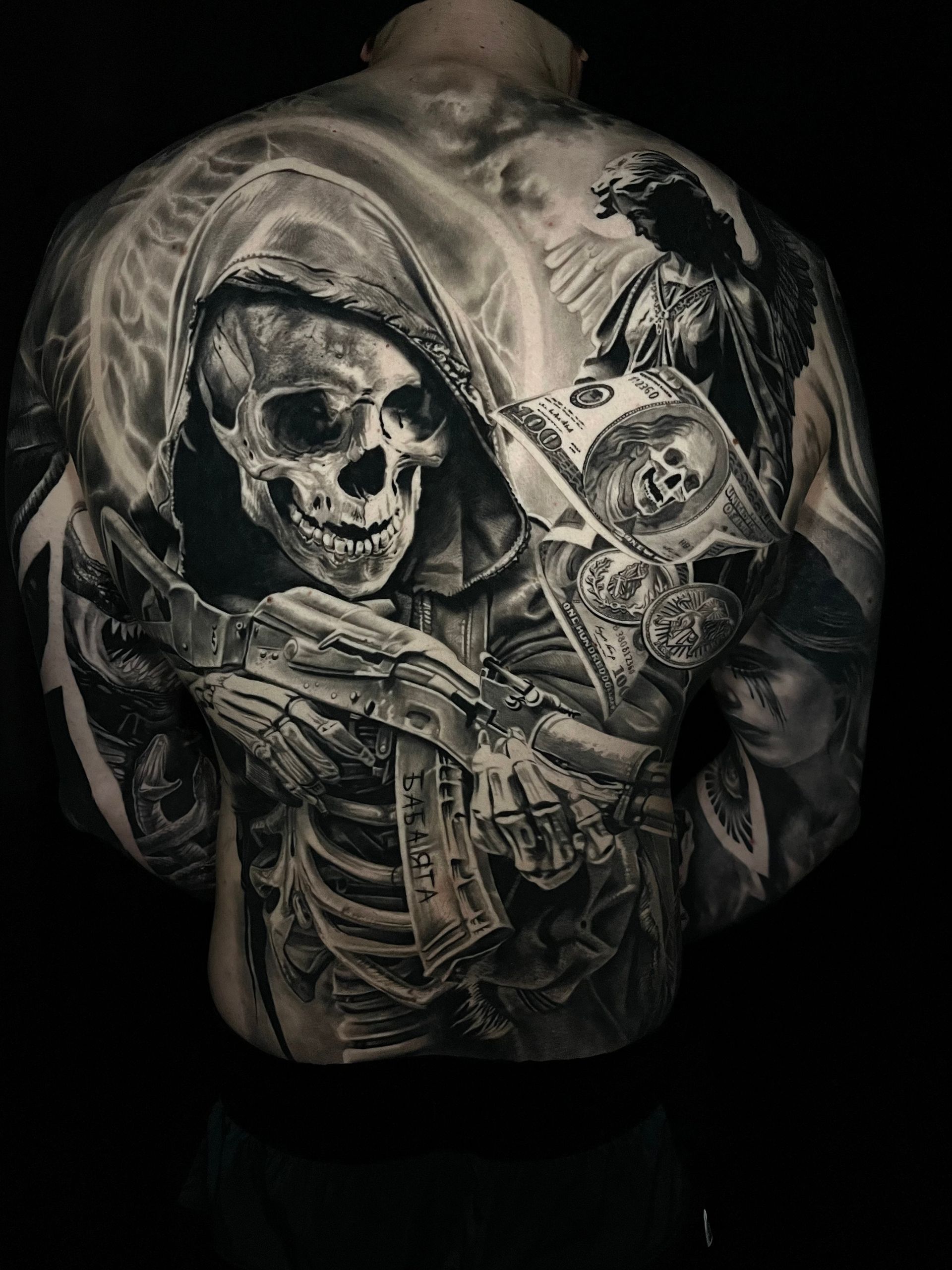 Ganzrücken-Tattoo eines Totenkopfes in Kapuzenmantel, der Geld und eine Pistole hält. Schwarz-weiß.