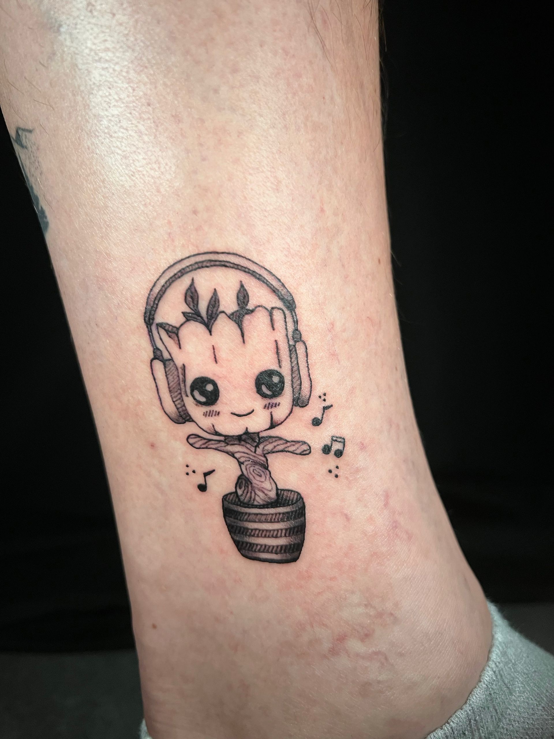 A small tattoo of a baby groot wearing headphones