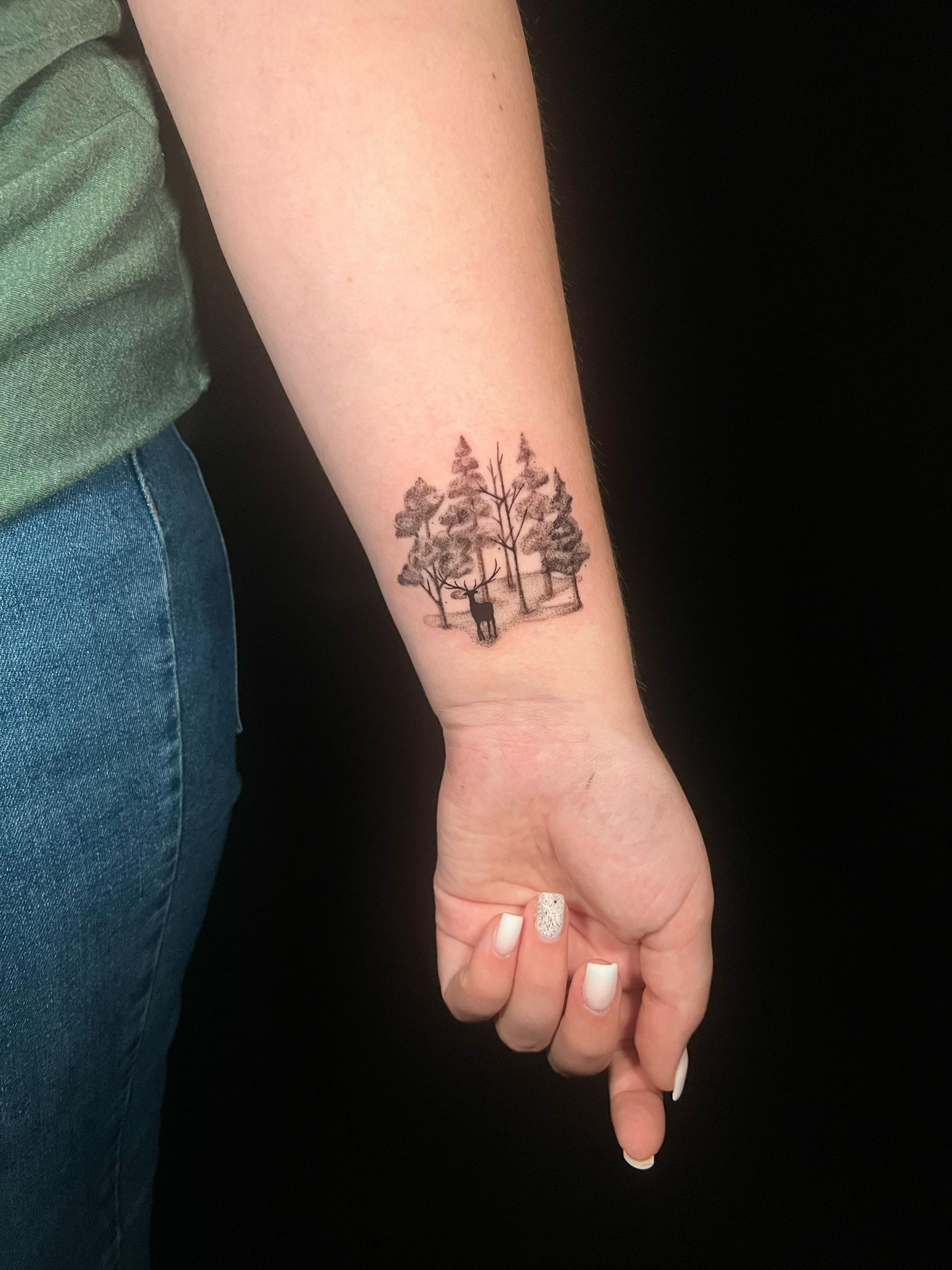A woman has a tattoo of a forest on her wrist.