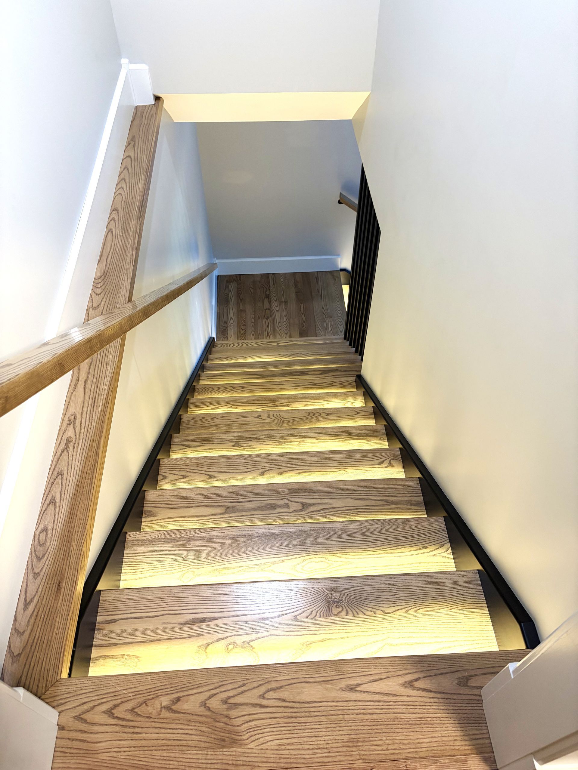 Wooden staircase with tread lights, descending to a lower level with wood handrail.