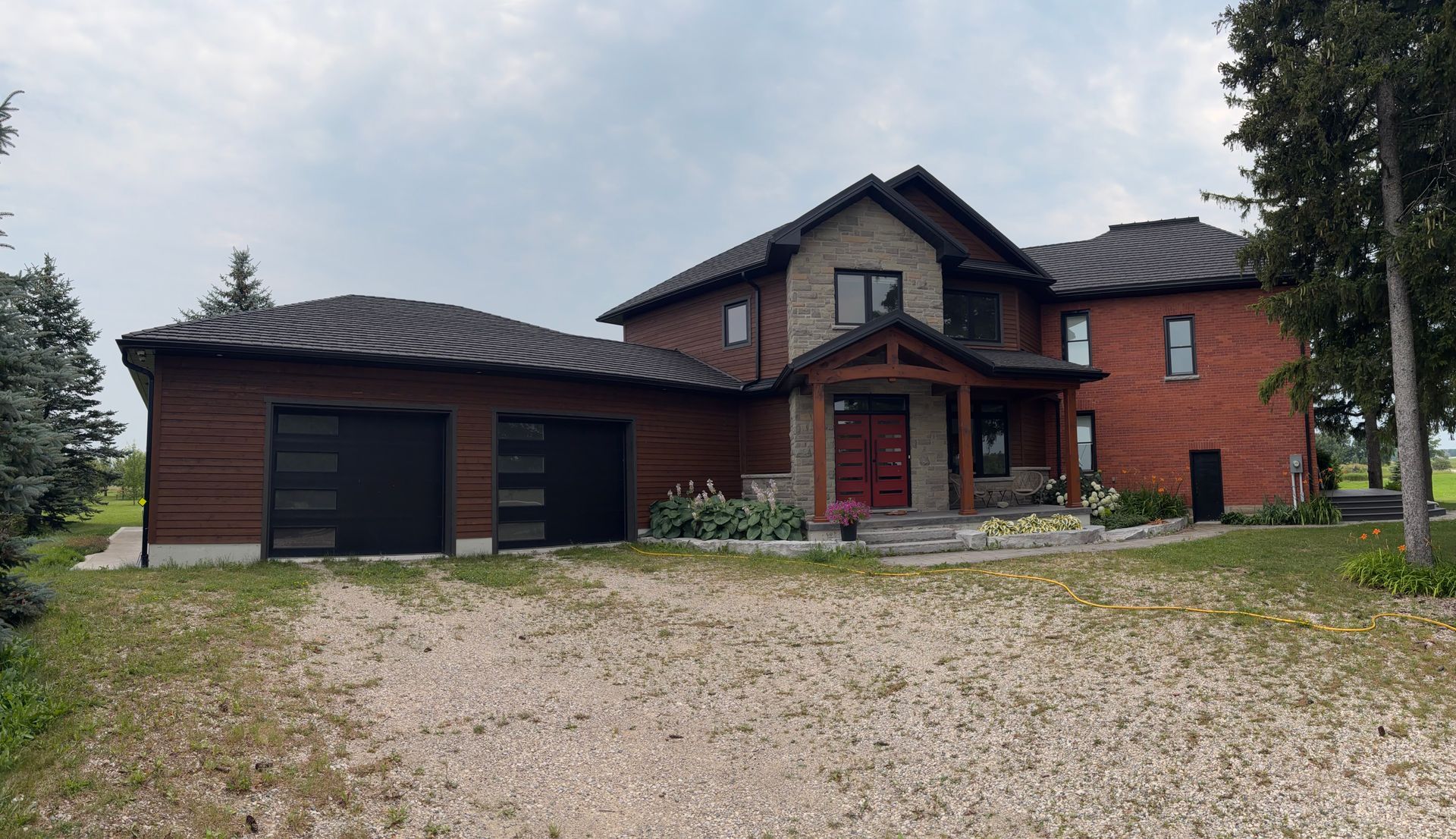 Modern brick house addition with dark roof, attached garage, and gravel driveway