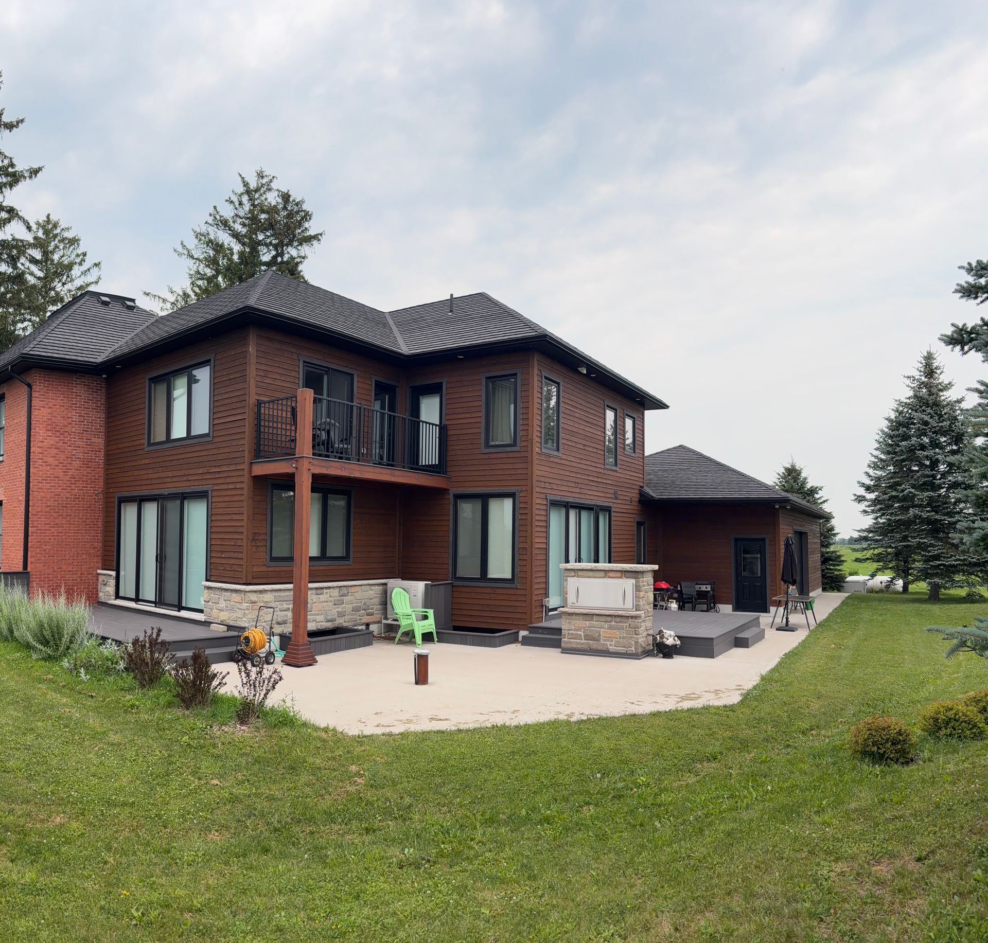 Modern two-story timber addition with balcony, concrete patio, and attached garage.