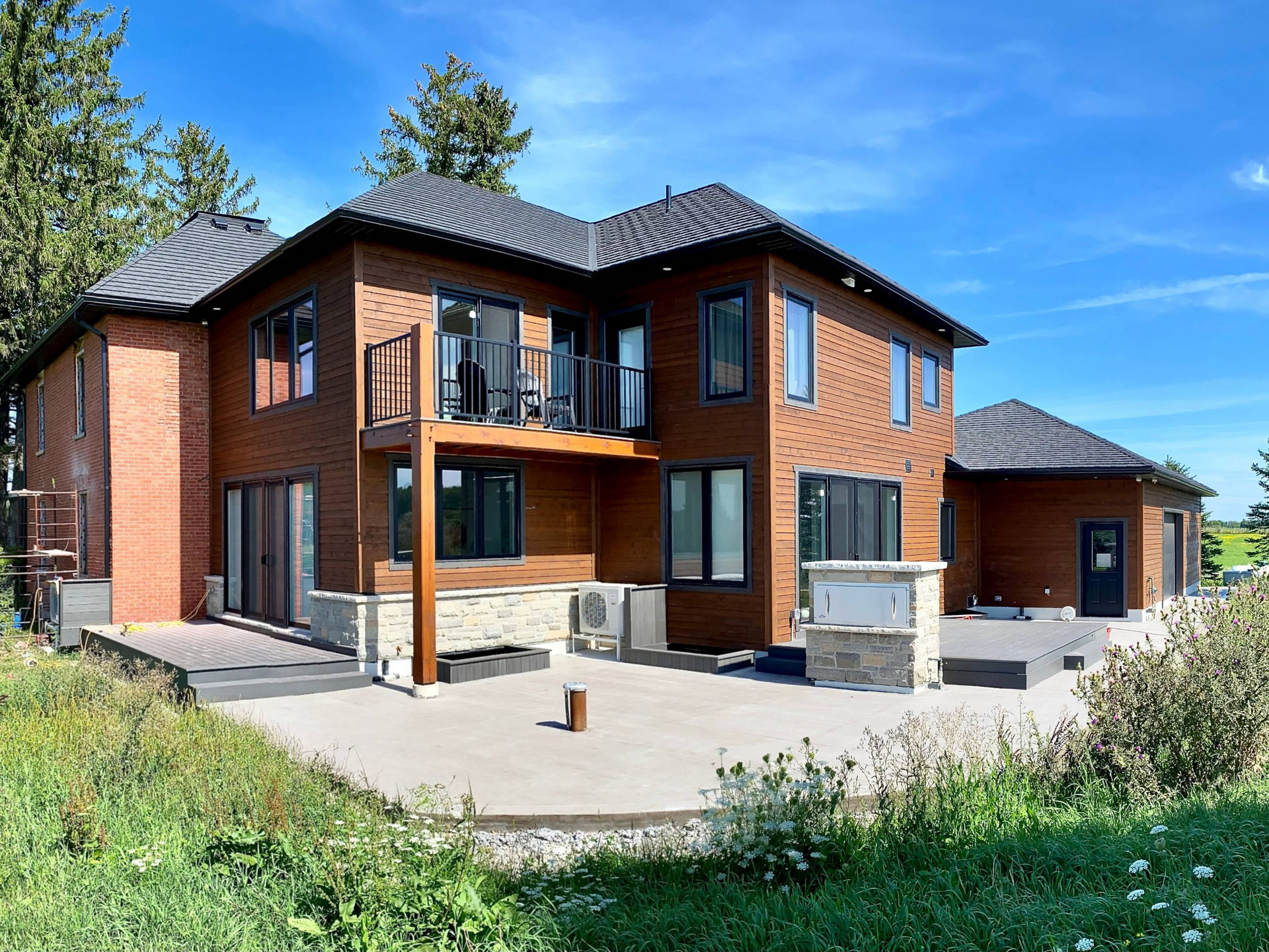 Modern two-story timber addition with balcony, concrete patio, and attached garage.